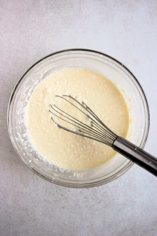 Top view of a glass bowl with a cream colour mixture and a hand whisk.
