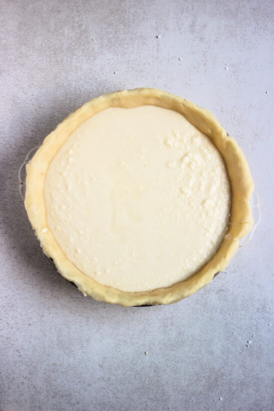 Top view of a round baking pie dish with raw dough and the ricotta filling.