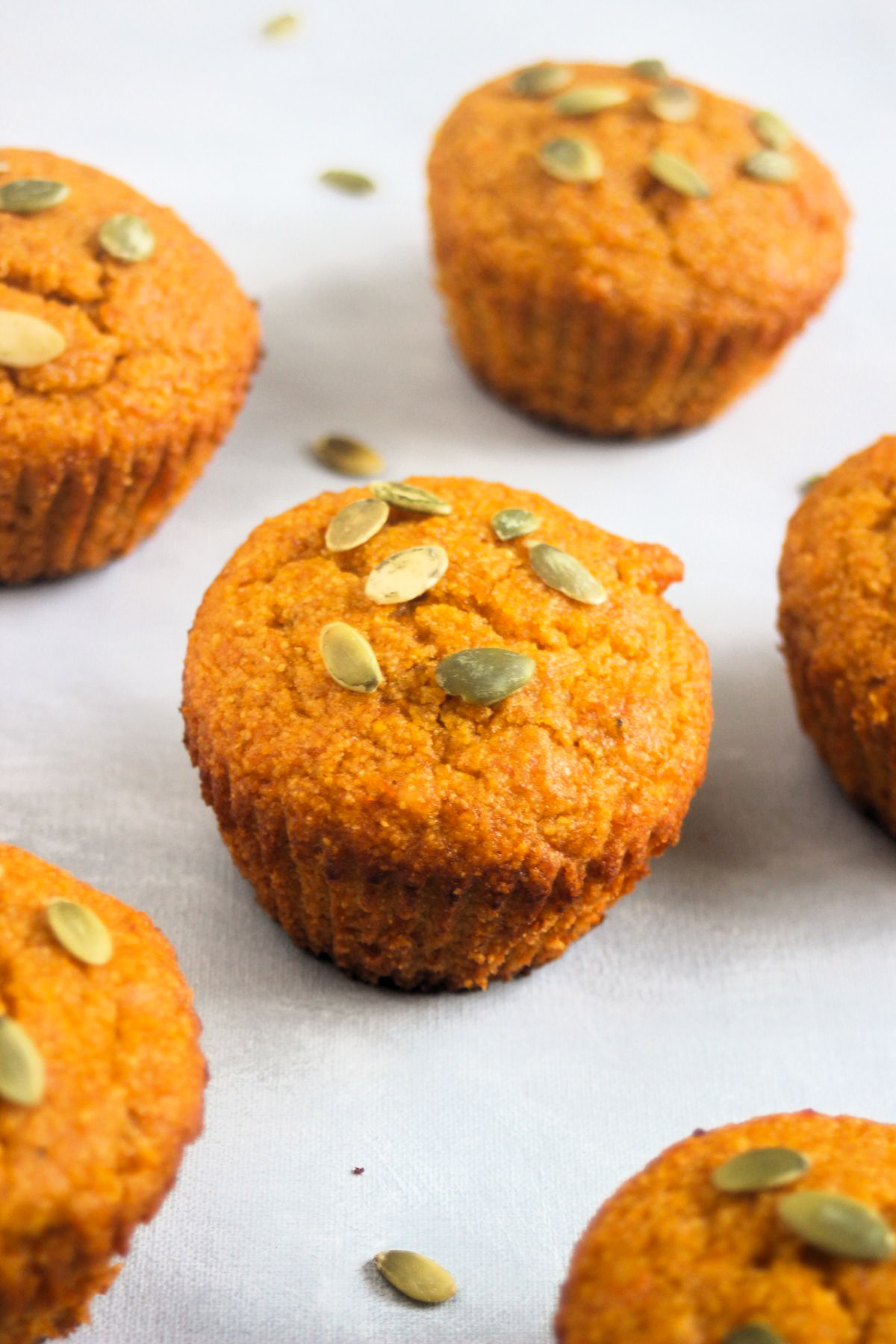 Pumpkin cornbread muffins with pumpkin seeds on a white surface.