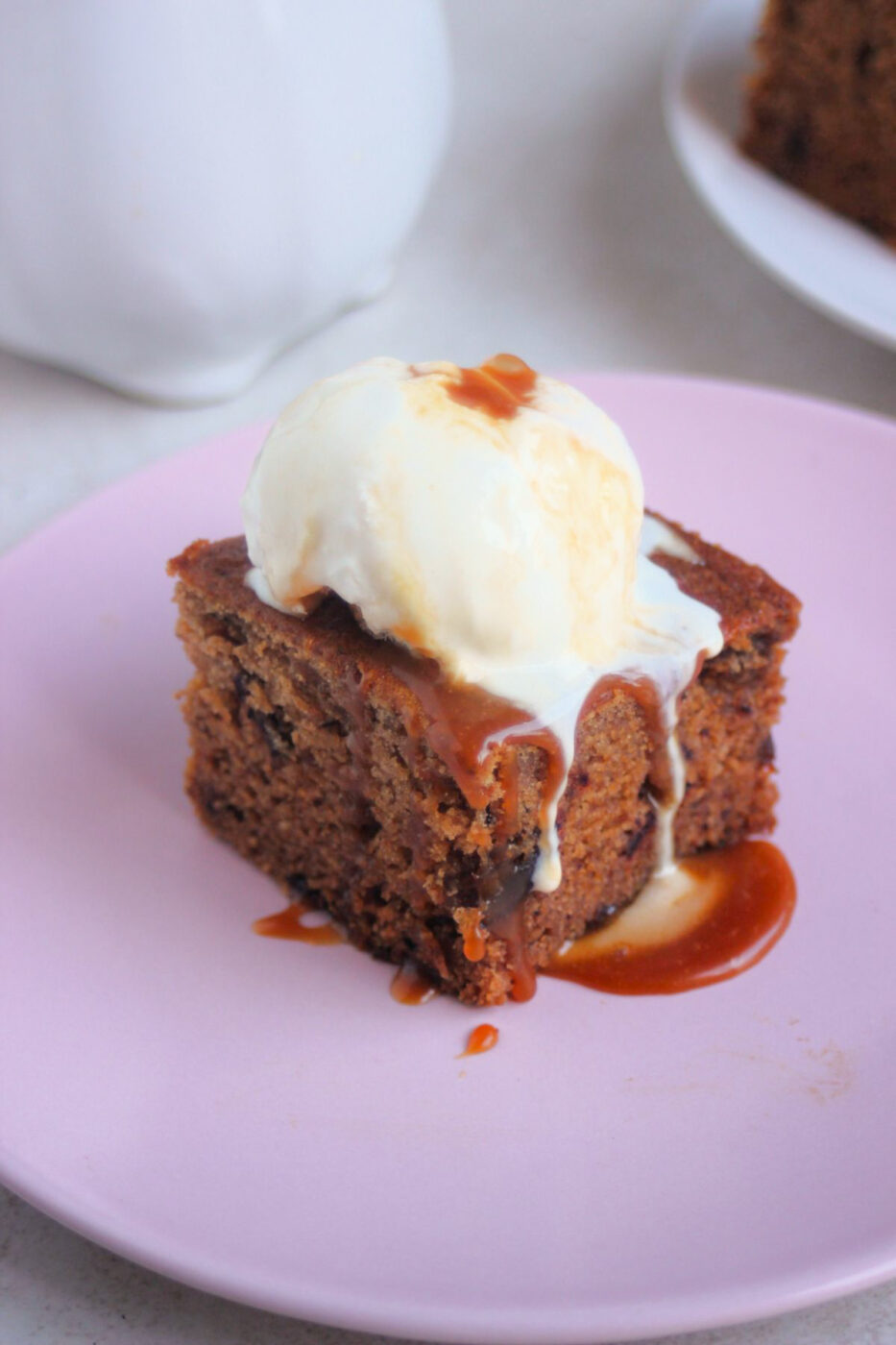 Portion of date cake topped with a scoop of ice cream and caramel sauce on a pink plate.