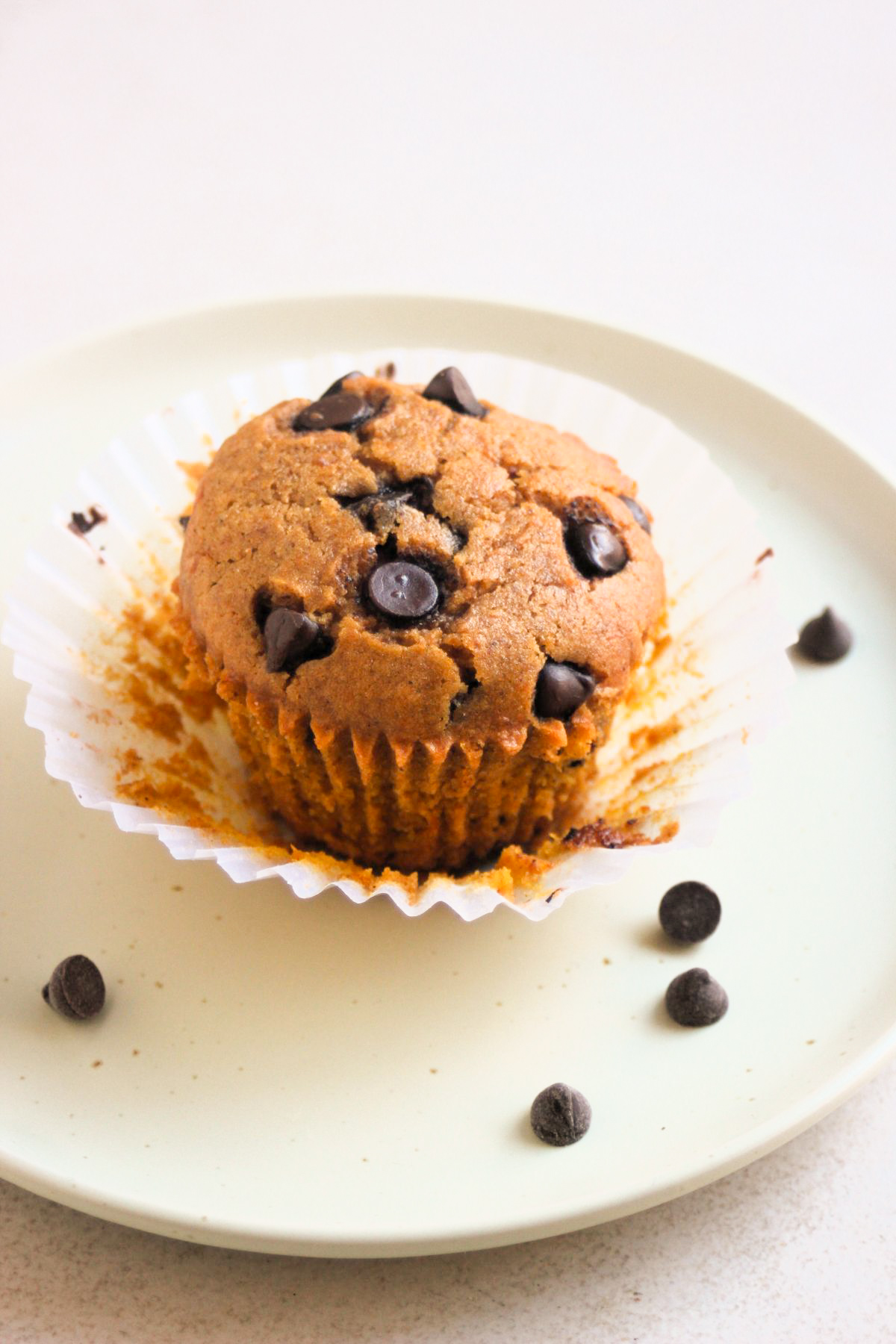 Pumpkin muffins with chocolate chips, with the liner open on a plate, and chocolate chips on the sides.