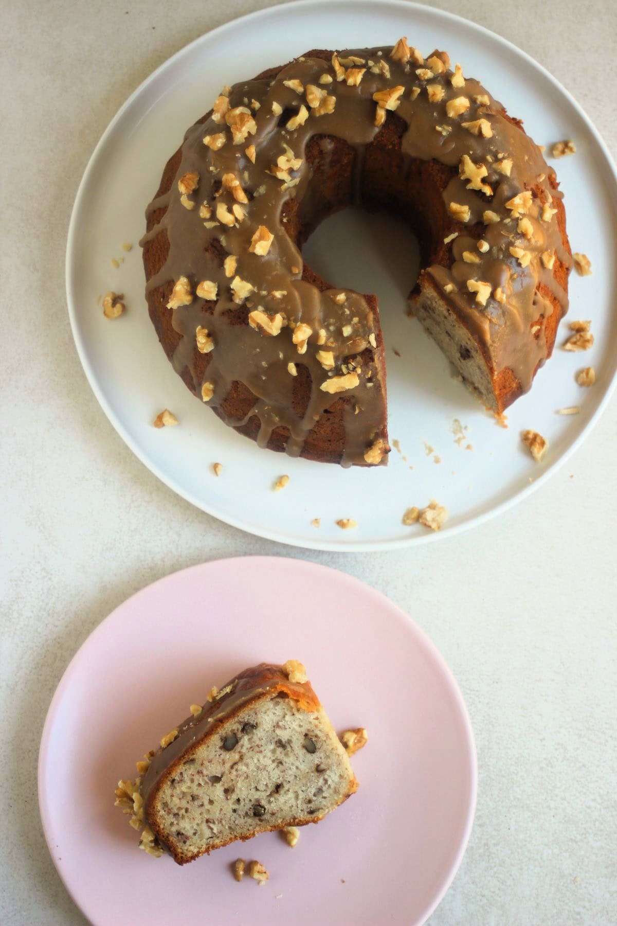 A Portion of banana bundt cake on a pink plate and banana bundt cake on a white plate seen from above.