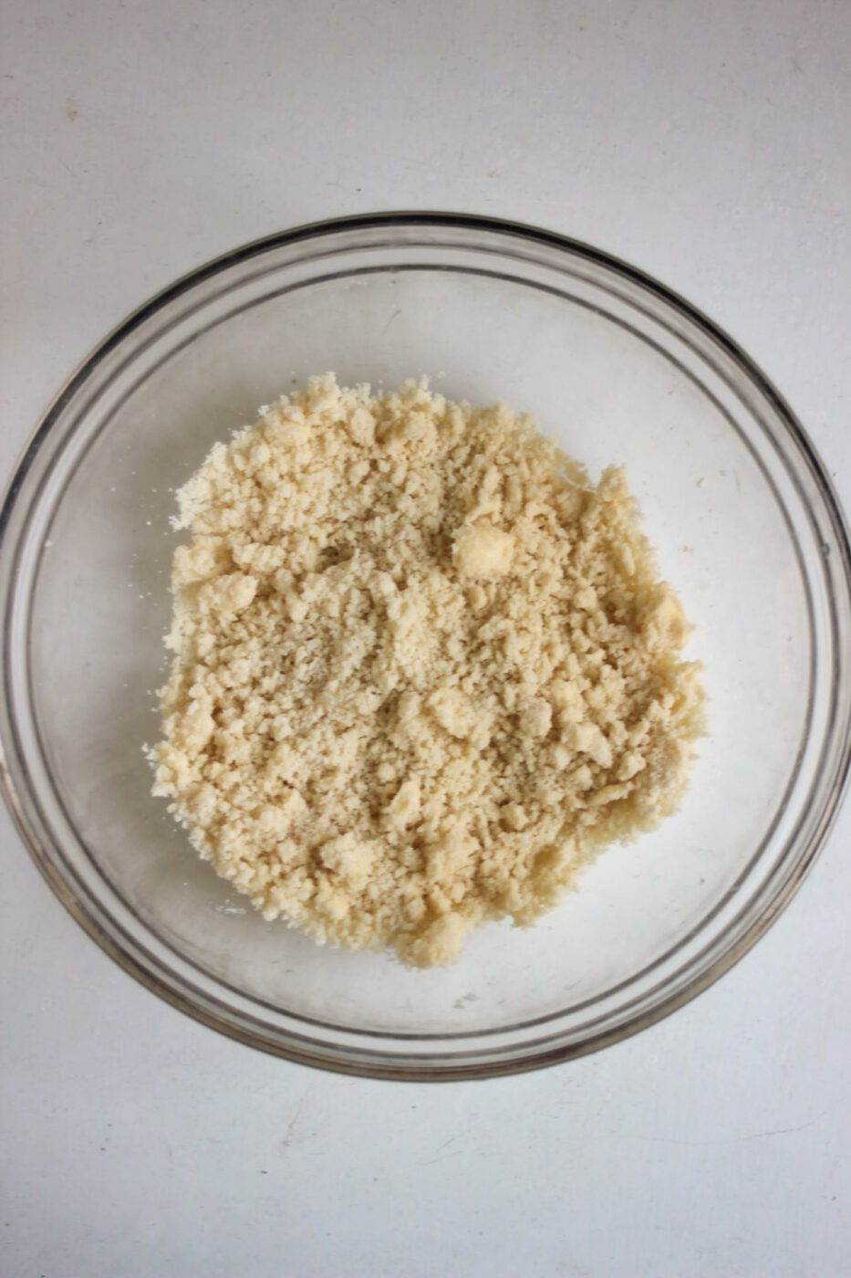 Glass bowl with crumbs on a white surface seen from above.