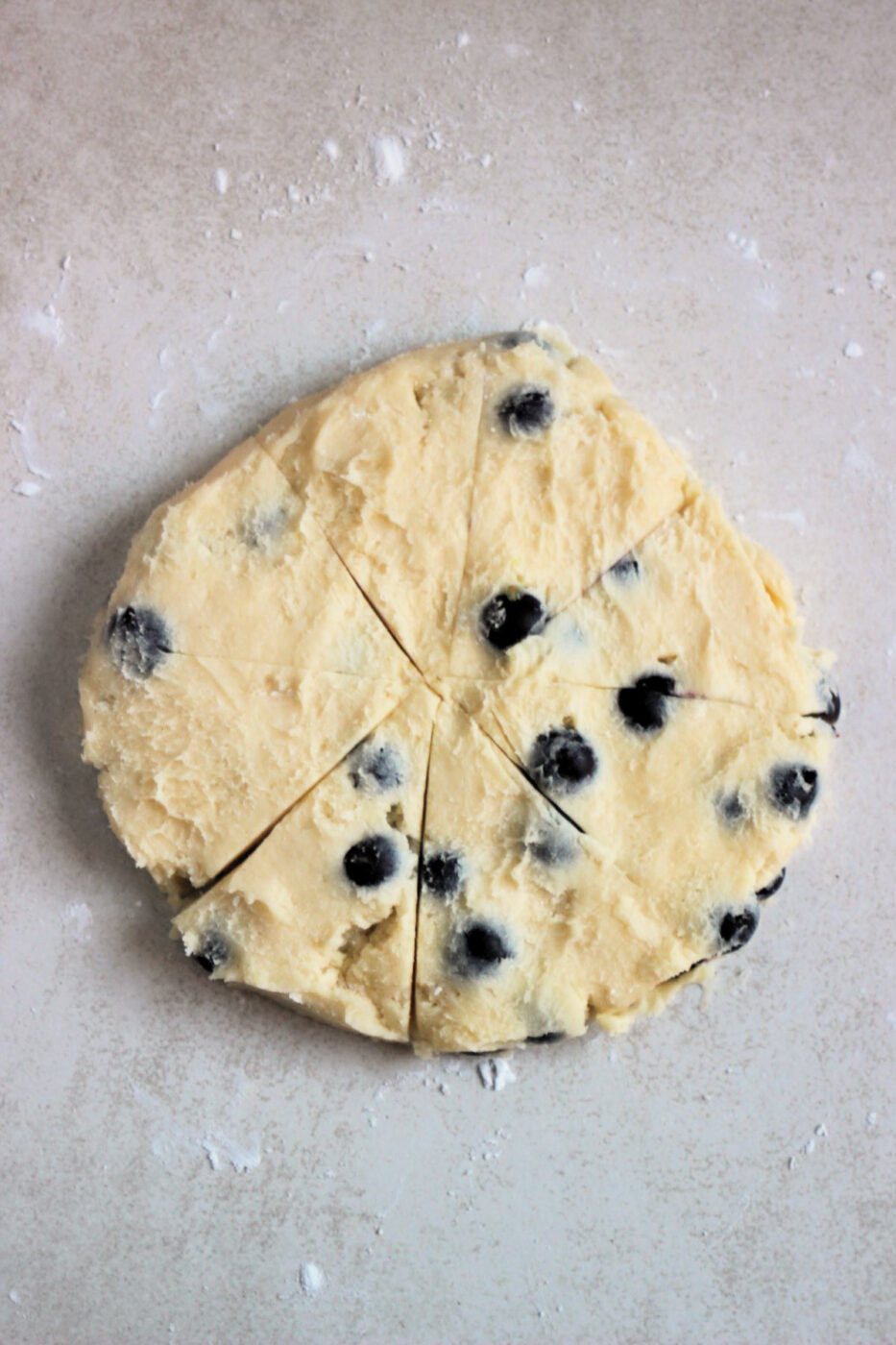Scone dough shaped round, cut into 8 triangles on a white surface, seen from above.
