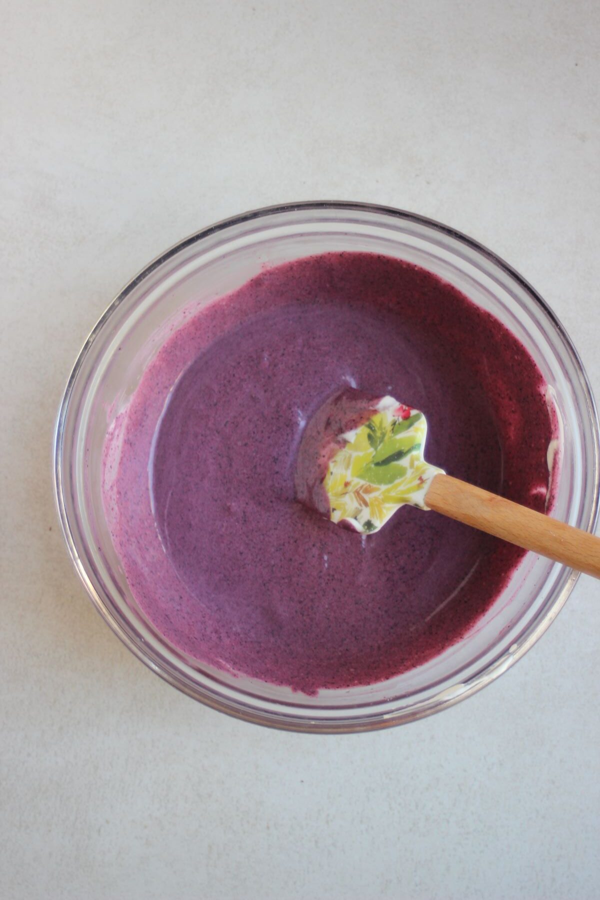 Glass bowl with a purple mixture and a rubber spatula.