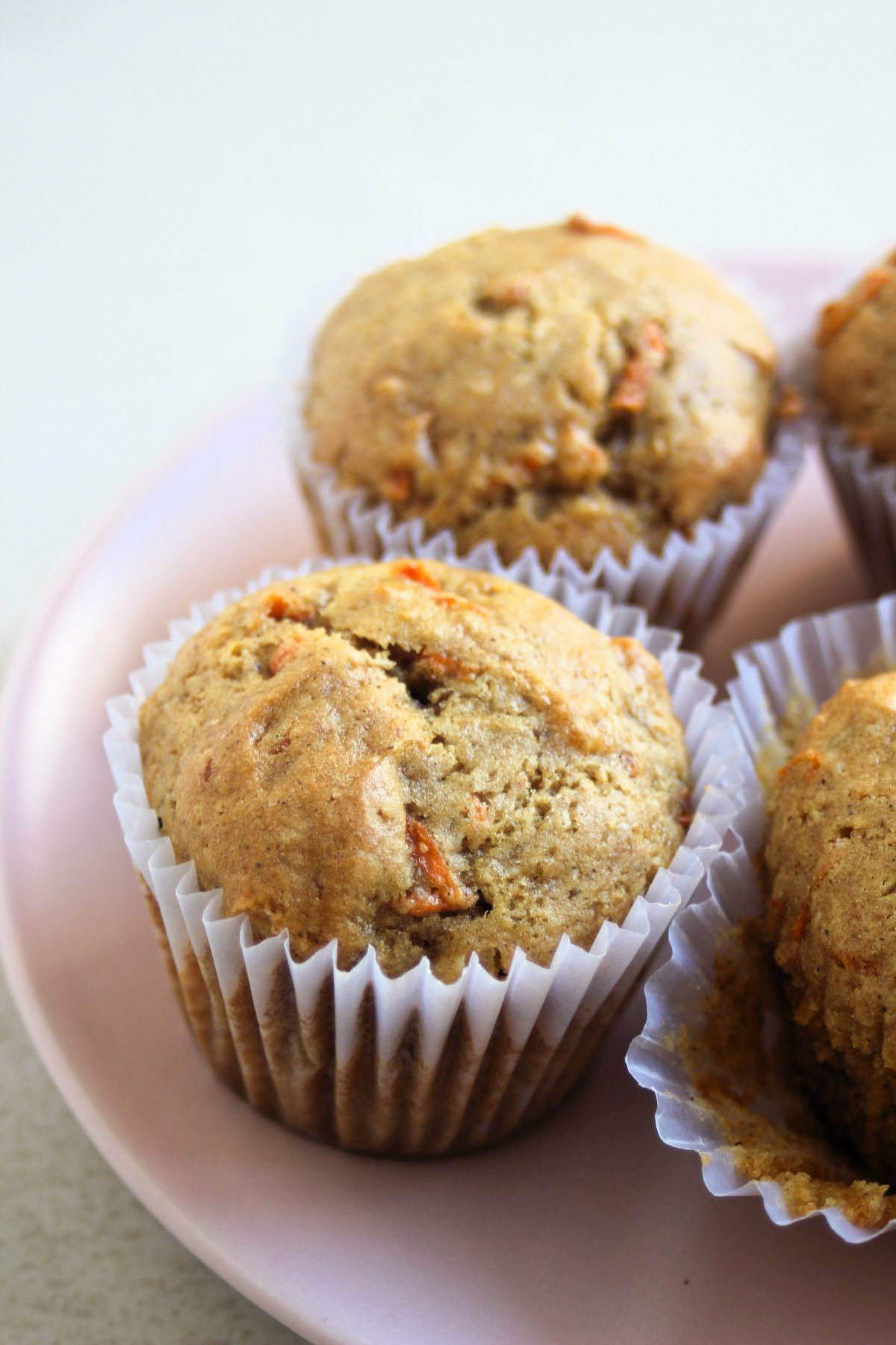 Carrot cake muffins in liners on a pink plate.