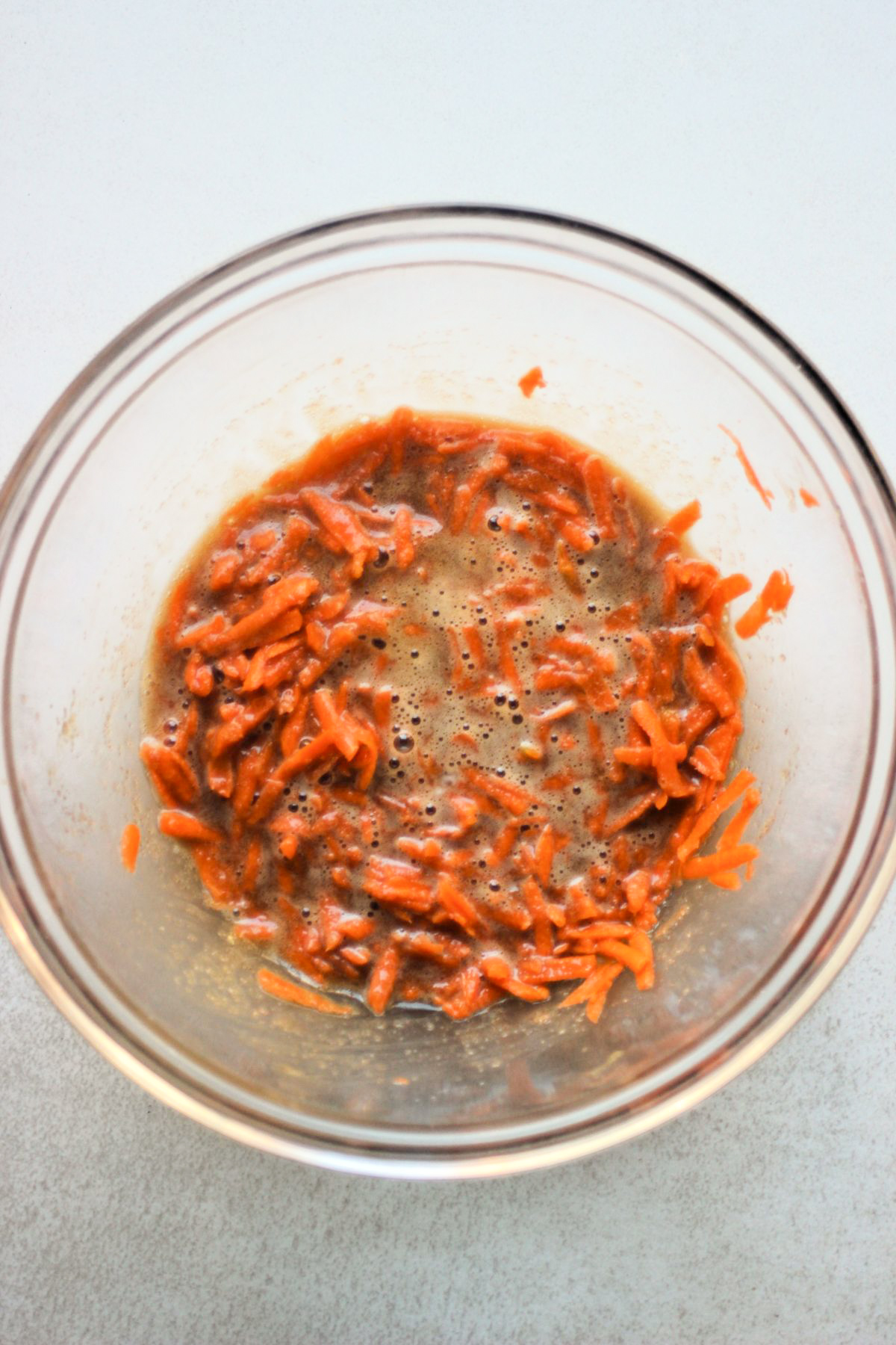 Glass bowl with a mixture that includes grated carrots.