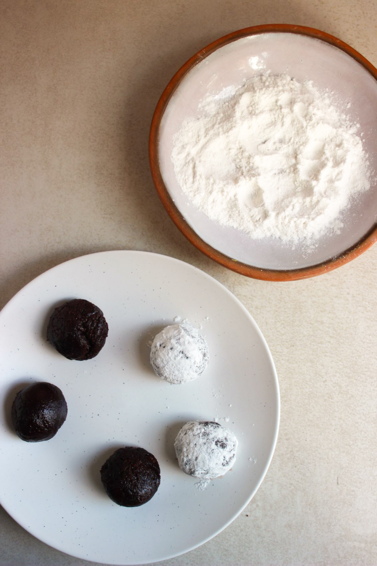 Plate with cookie dough balls, two coated with powdered sugar.