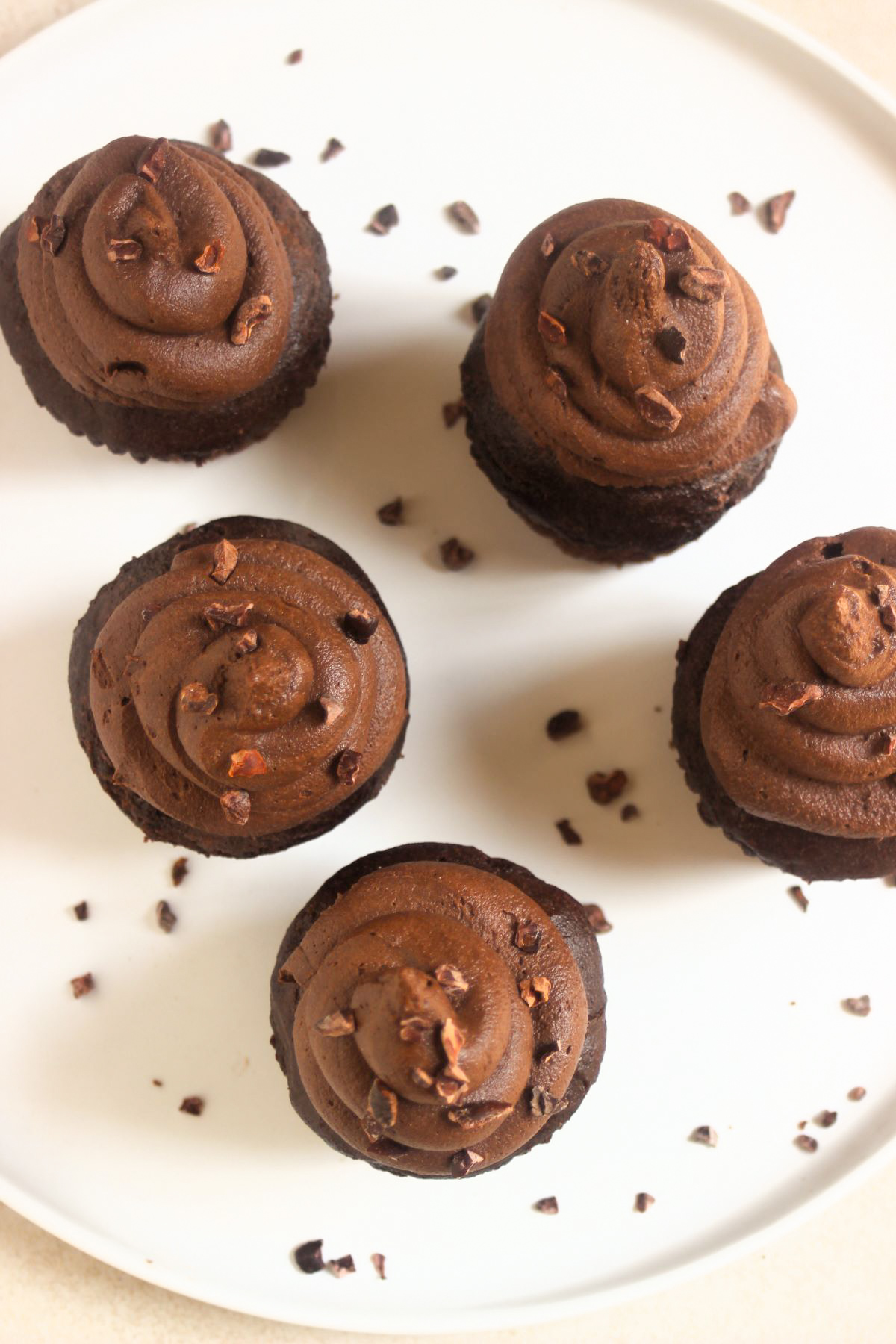 Chocolate cupacakes with cocoa nibs on a white plate seen from above.