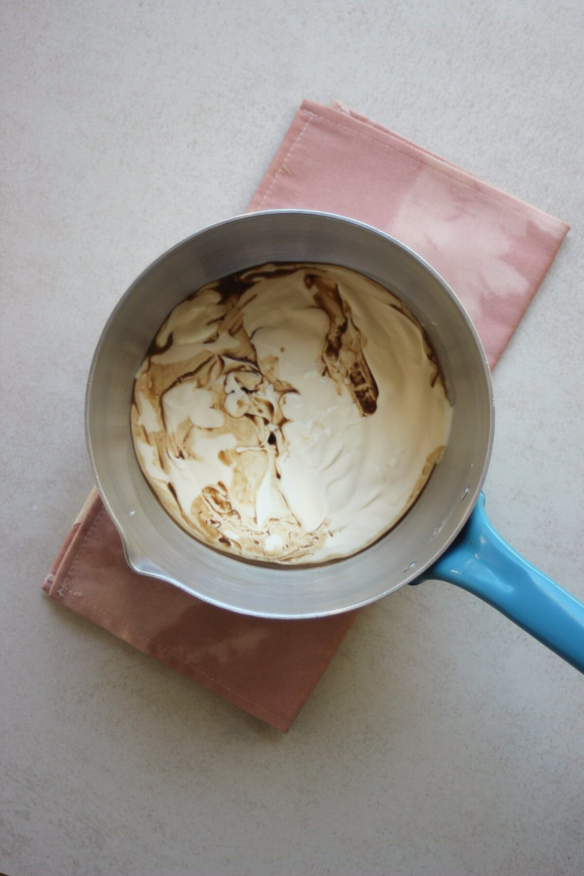 Deep saucepan with cream and vanilla extract. Pink napkin under the saucepan.