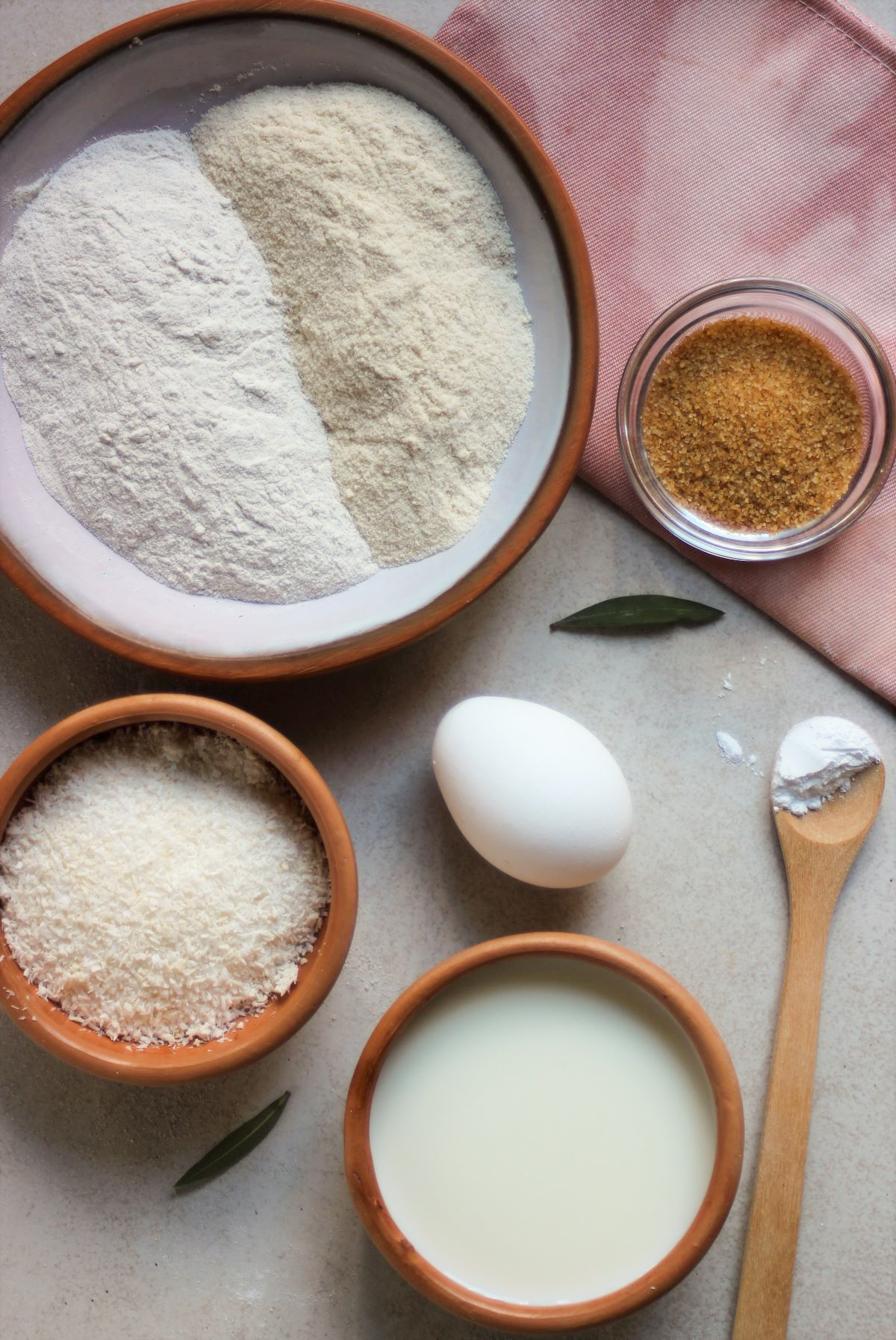 Coconut pancakes ingredients and a pink napkin on a white surface seen from above.