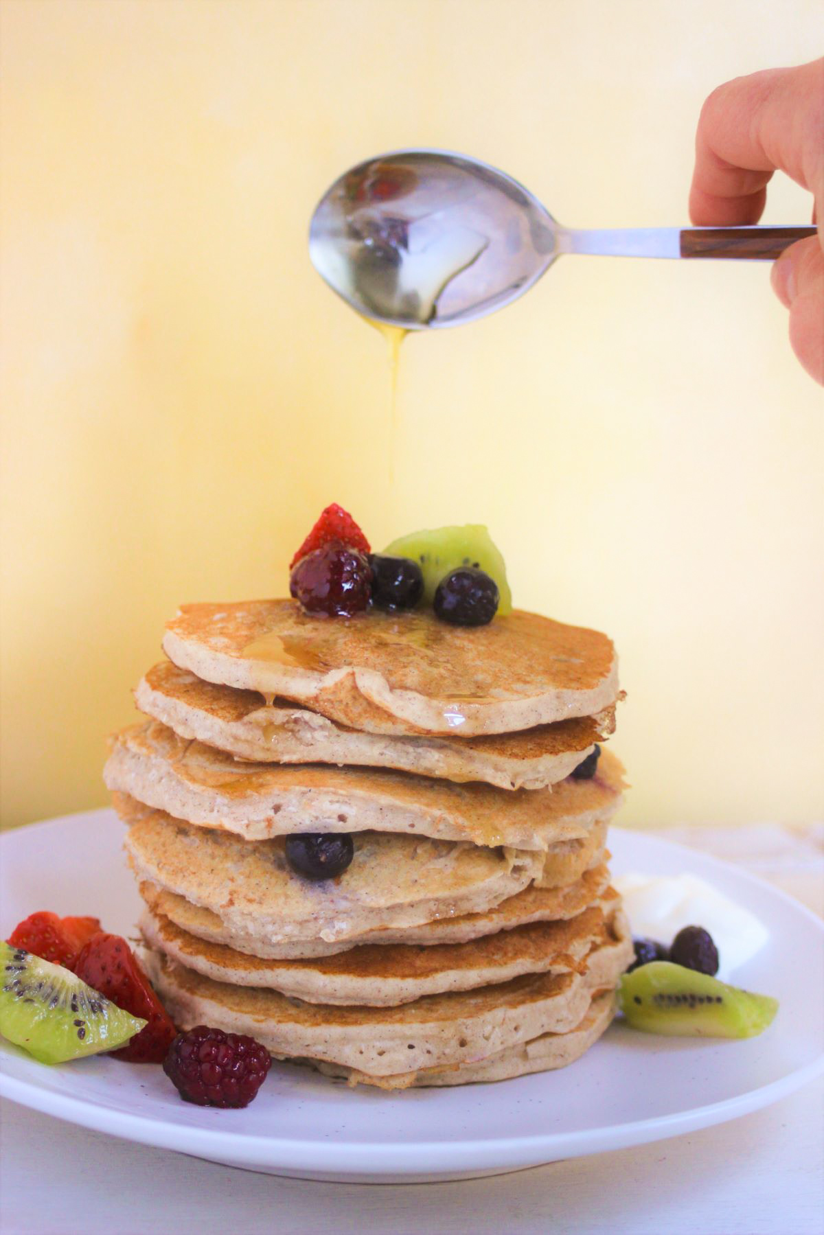 Stack pancakes with fresh fruits and a spoon throwing honey to it.