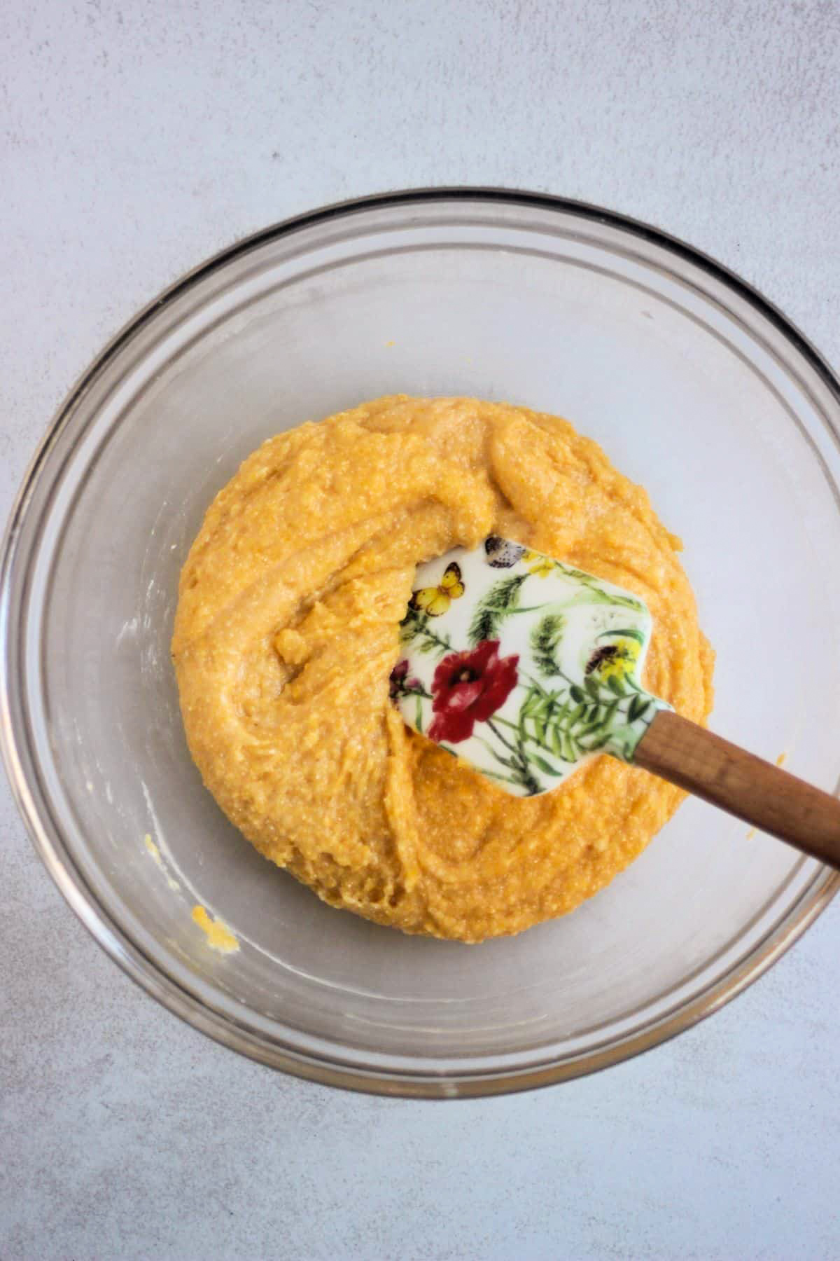 Glass bowl with a yellow mixture and a rubber spatula.