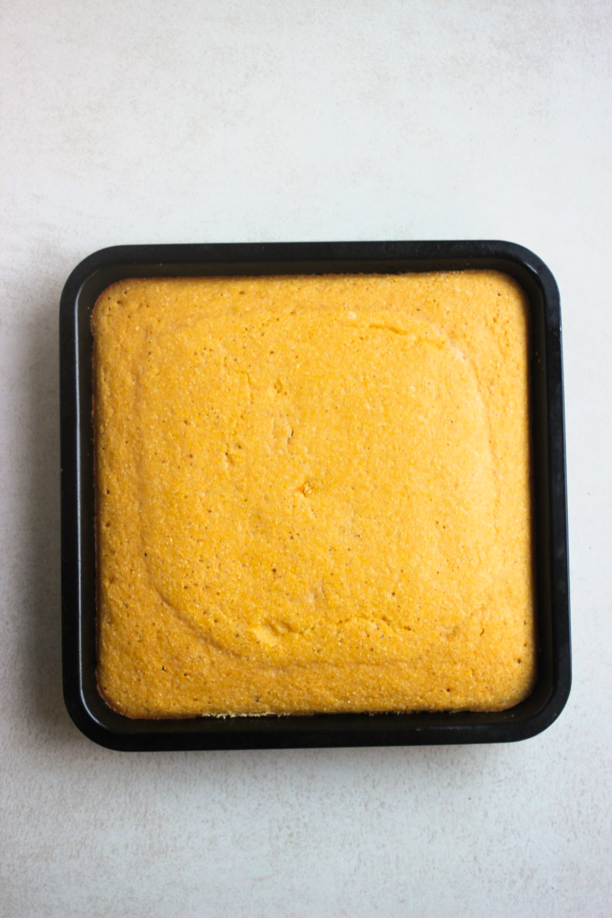 Cornbread on a square baking pan on a white surface, seen from above.