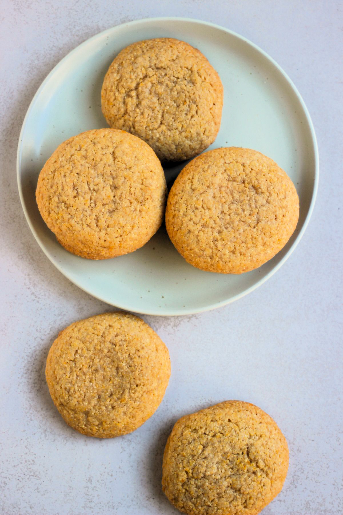 Cornmeal cookies on an aqua-green plate, and others beside on a white surface, seen from above.