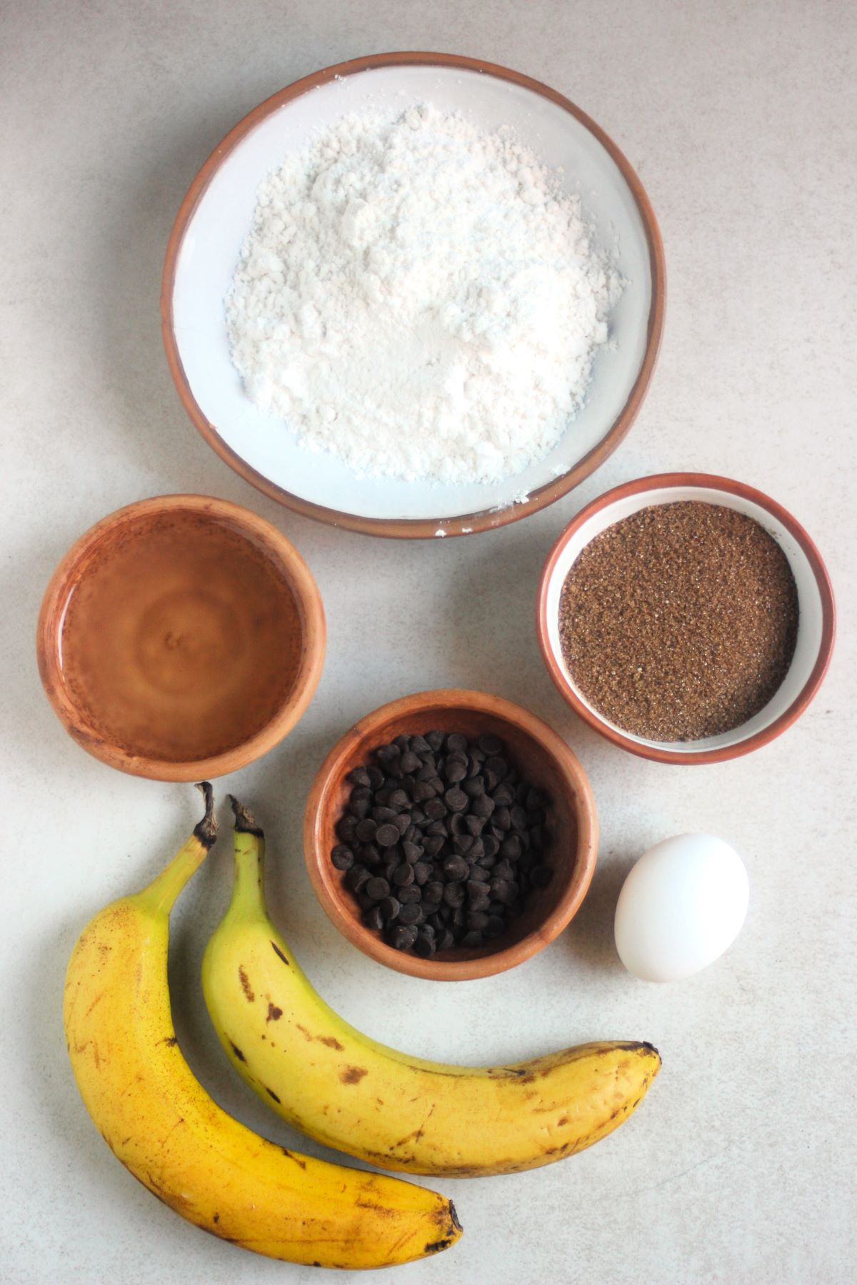 Banana muffins ingredients on a white surface seen from above.