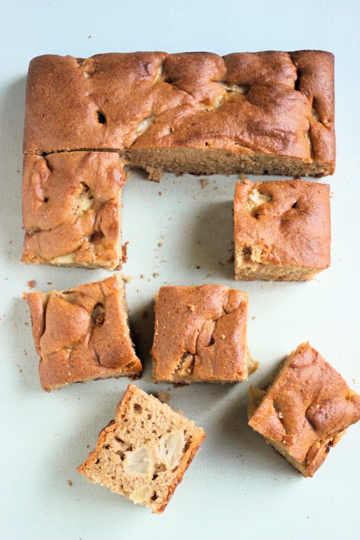 Top view of apple cake with five portions cut out, on a light sky blue surface.