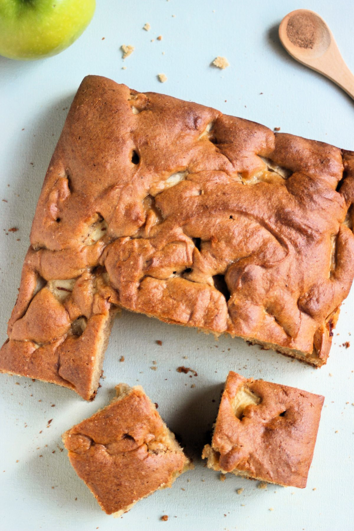Top view of apple cake with two portions cut out, on a light sky blue surface.