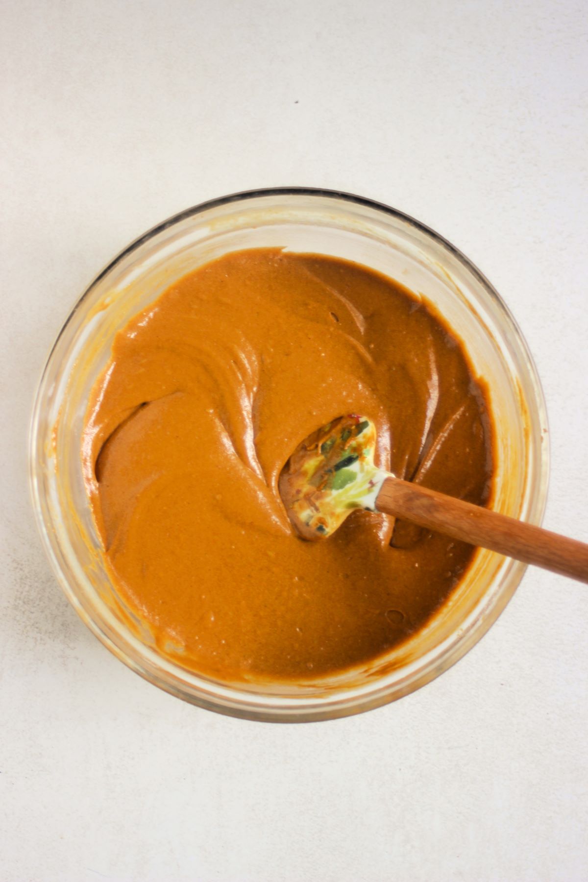 Glass bowl with a smooth caramel colour mixture and a rubber spatula.