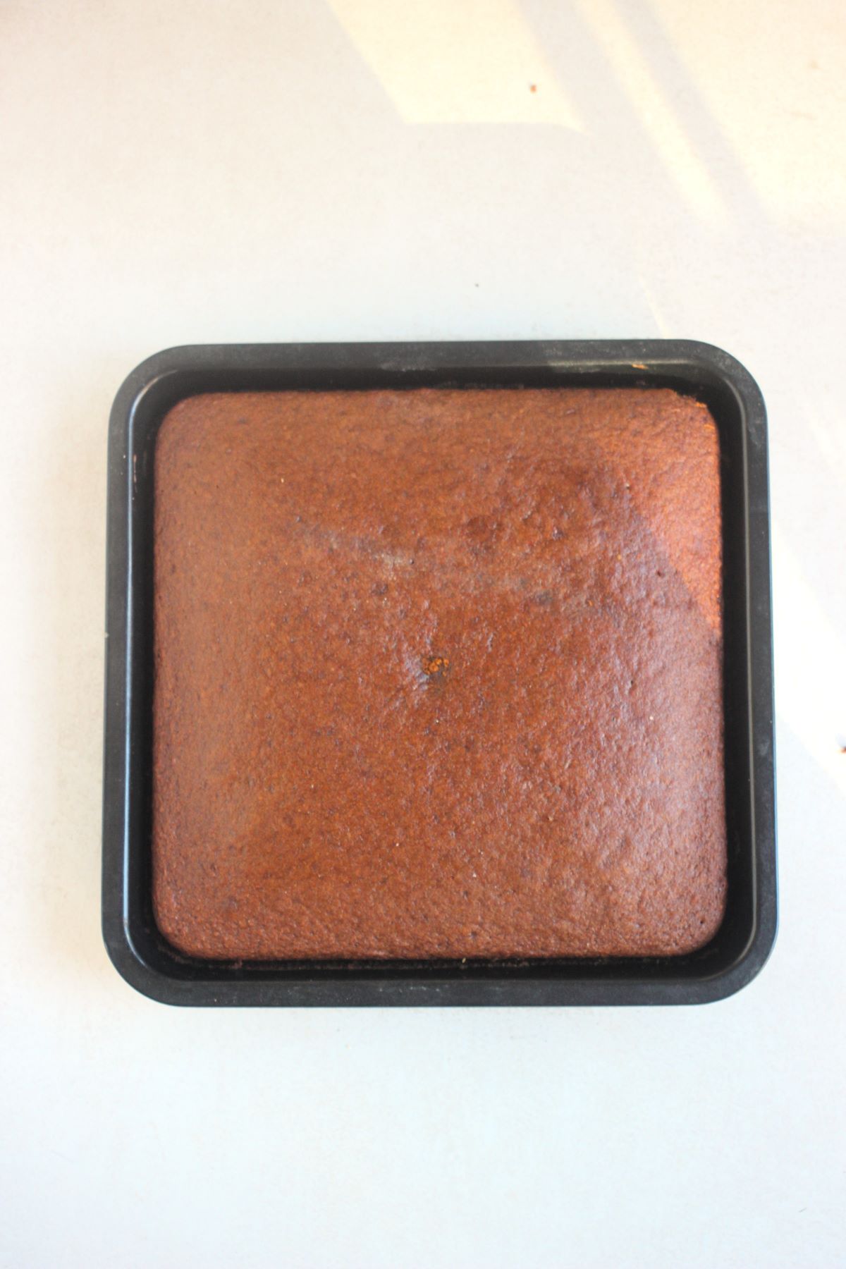 Square pan with gingerbread cake on a white surface seen from above.
