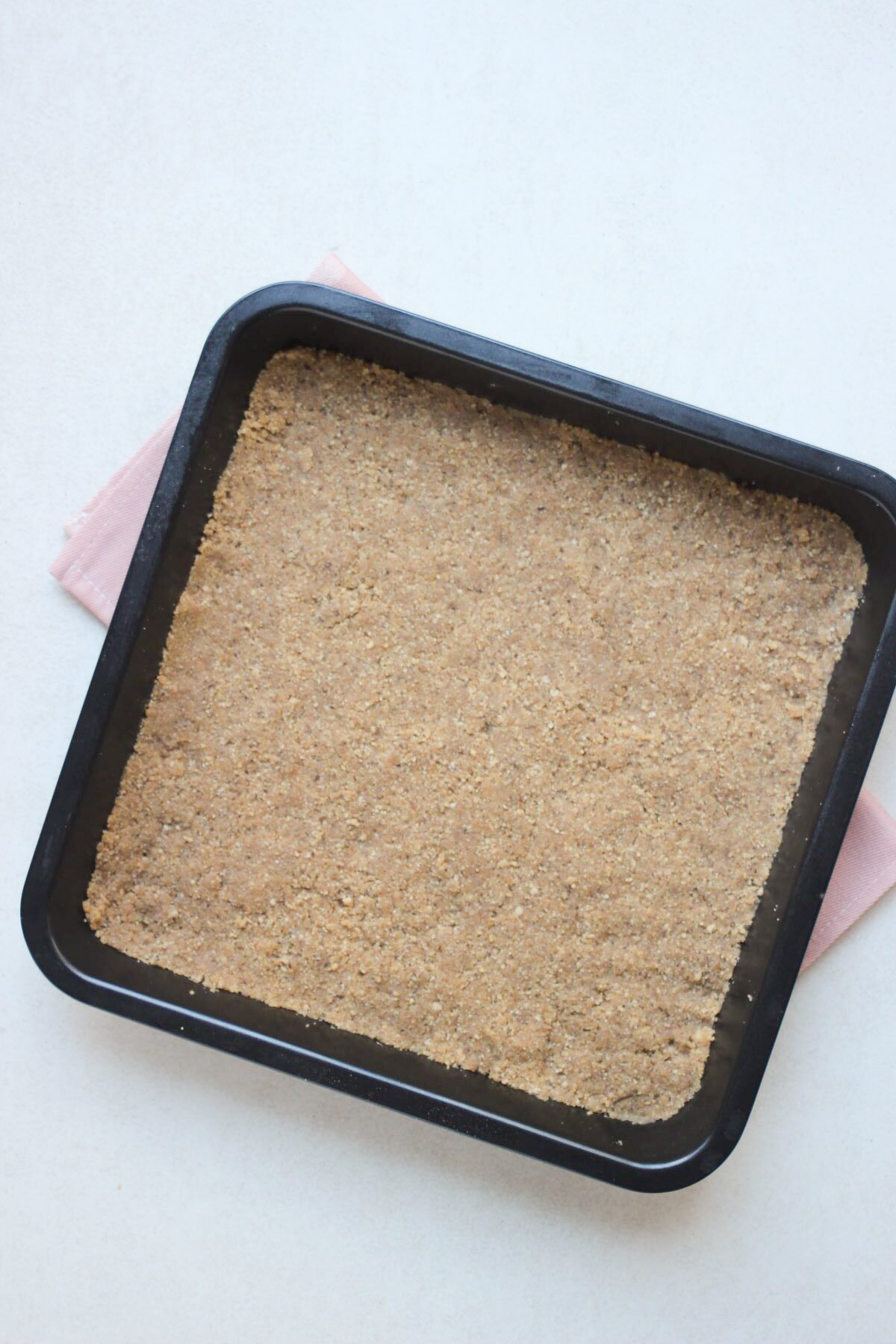 Square baking pan with a cookie base. Pink napkin under the pan.