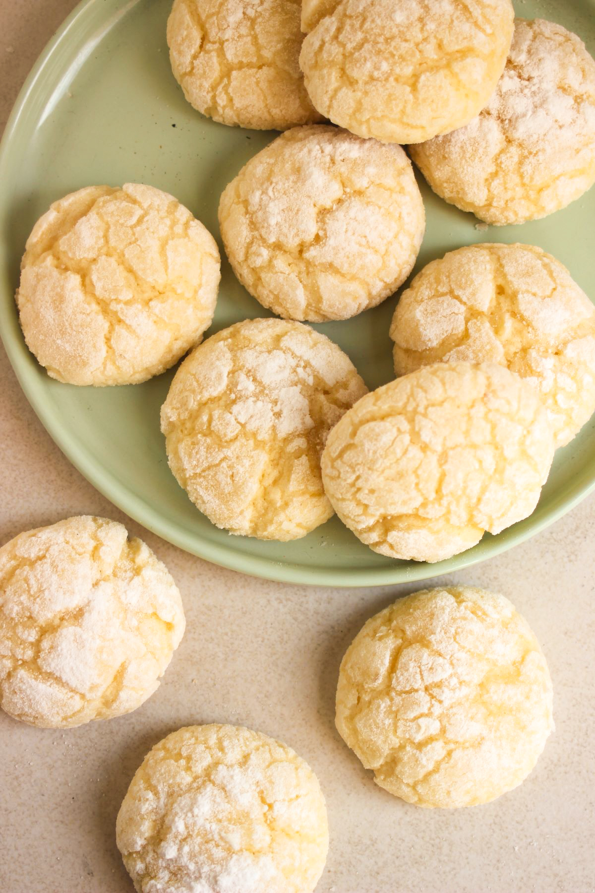 Lemon crinkle cookies on a plate and more cookies beside seen from above.