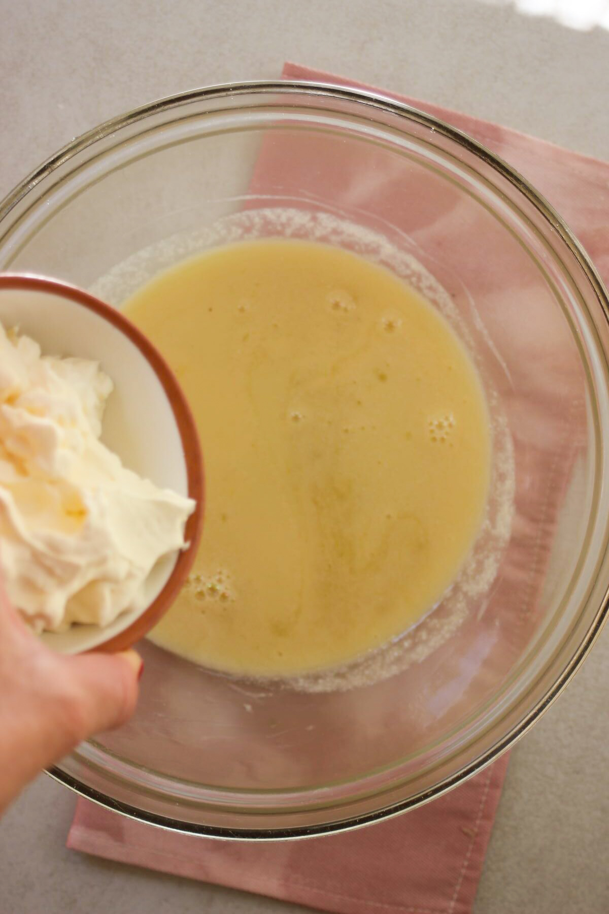 A tiny bowl with cream is about to be poured into a glass bowl with a liquid.