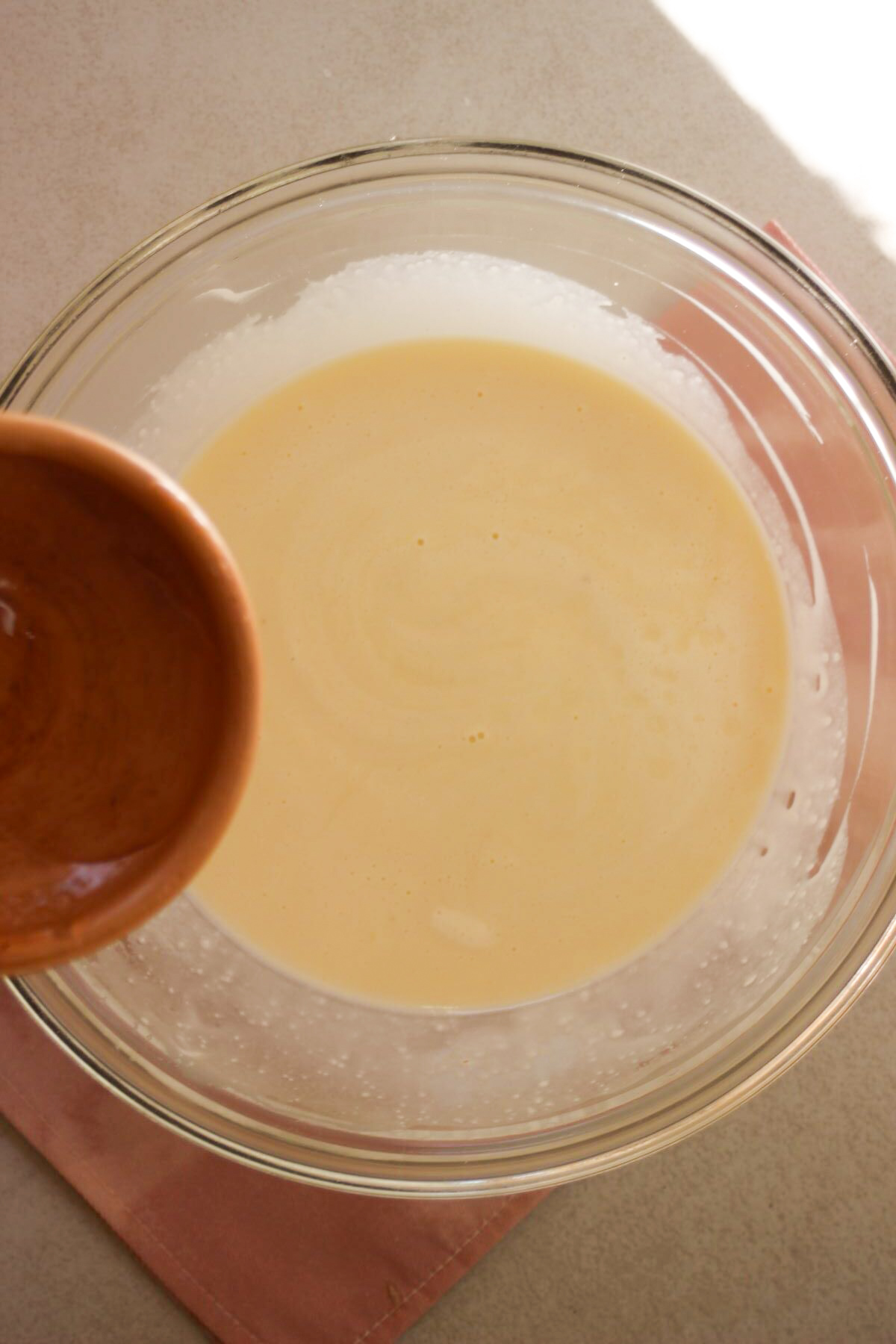 A bowl of liquid is about to be poured into a glass bowl with a mixture.