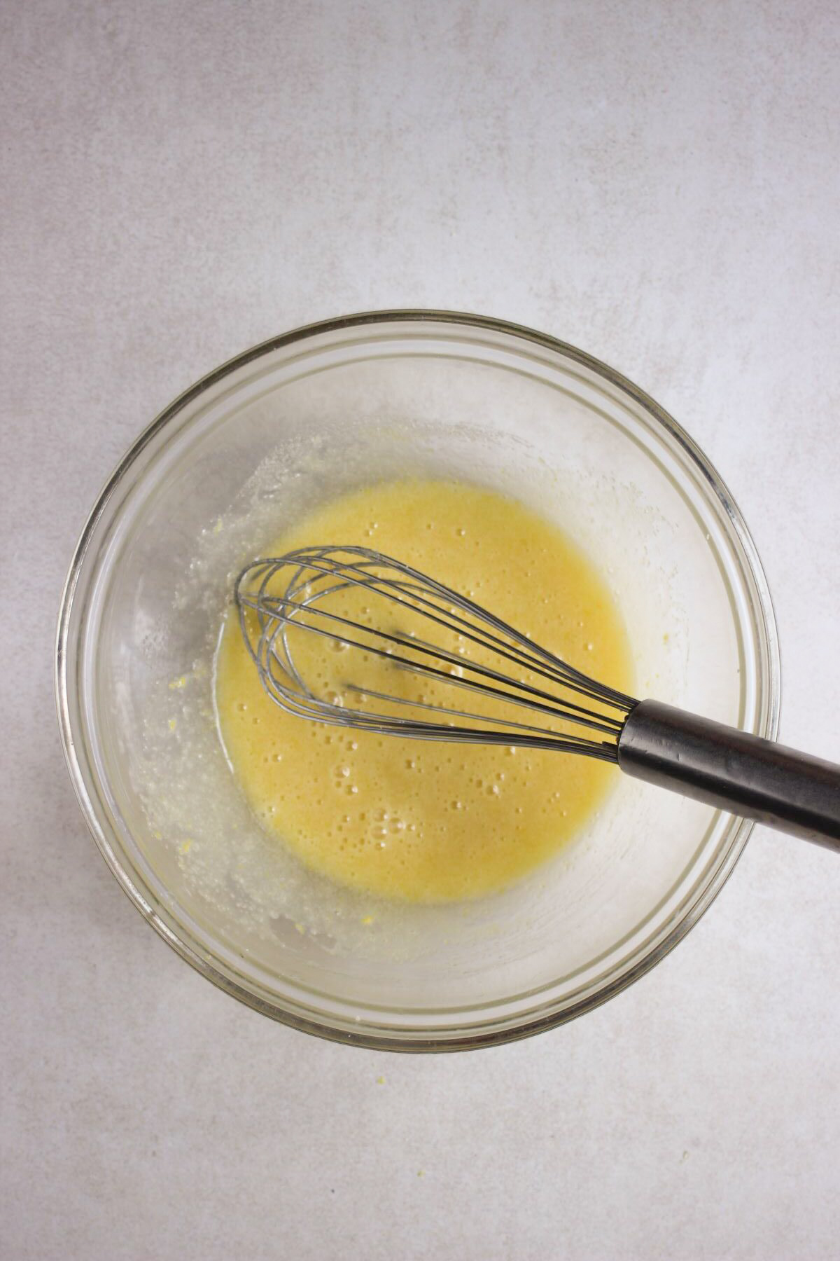 Glass bowl with a yellow liquid and a hand whisk.