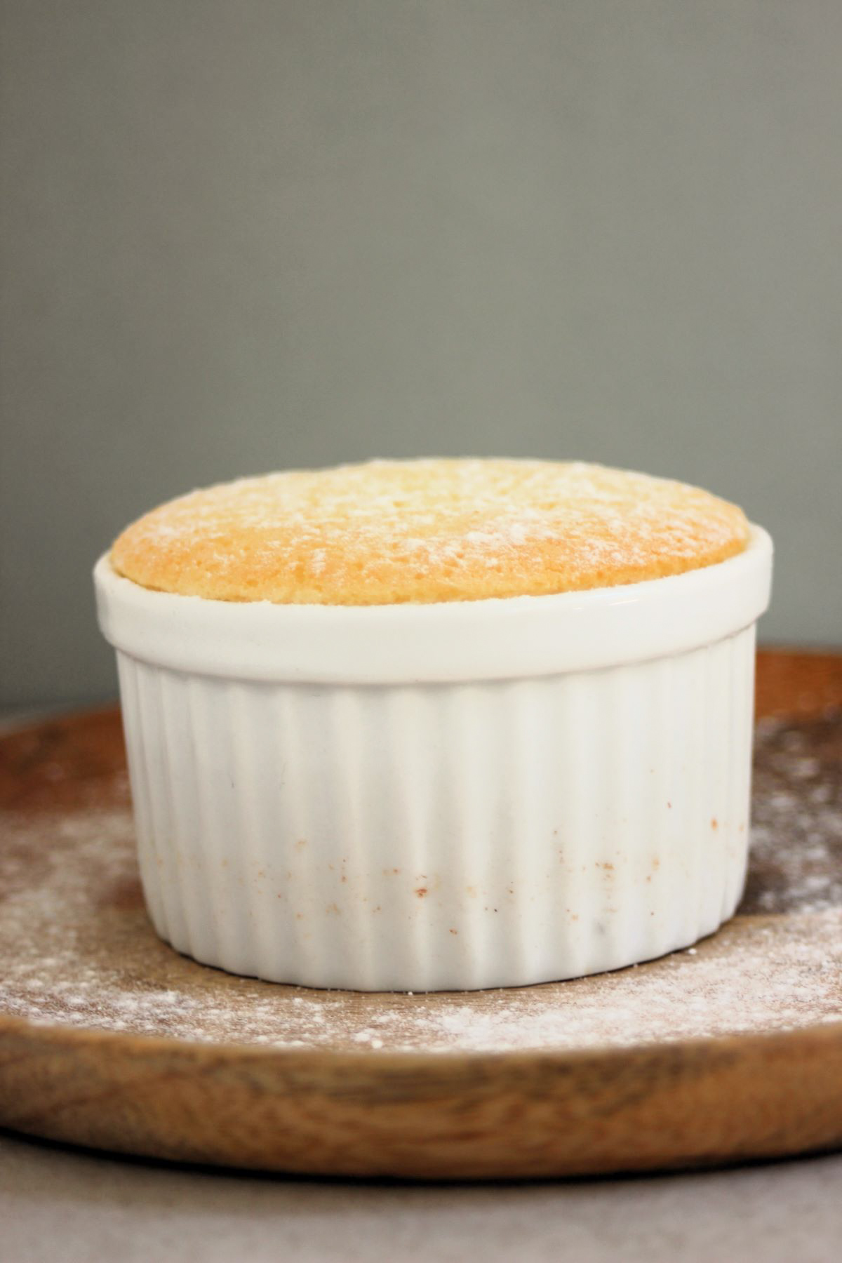 White ramekin with lemon pudding cake on a wooden plate.