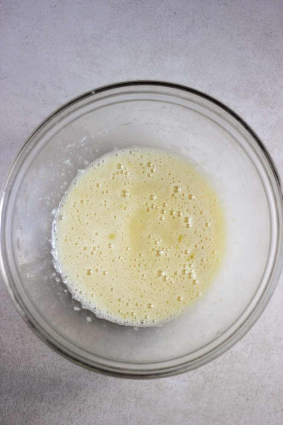 Glass bowl with a light yellow liquid on a white surface.