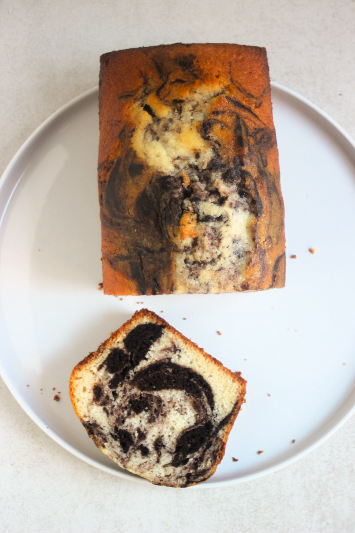 Marble loaf cake and a slice of it on a white plate seen from above.