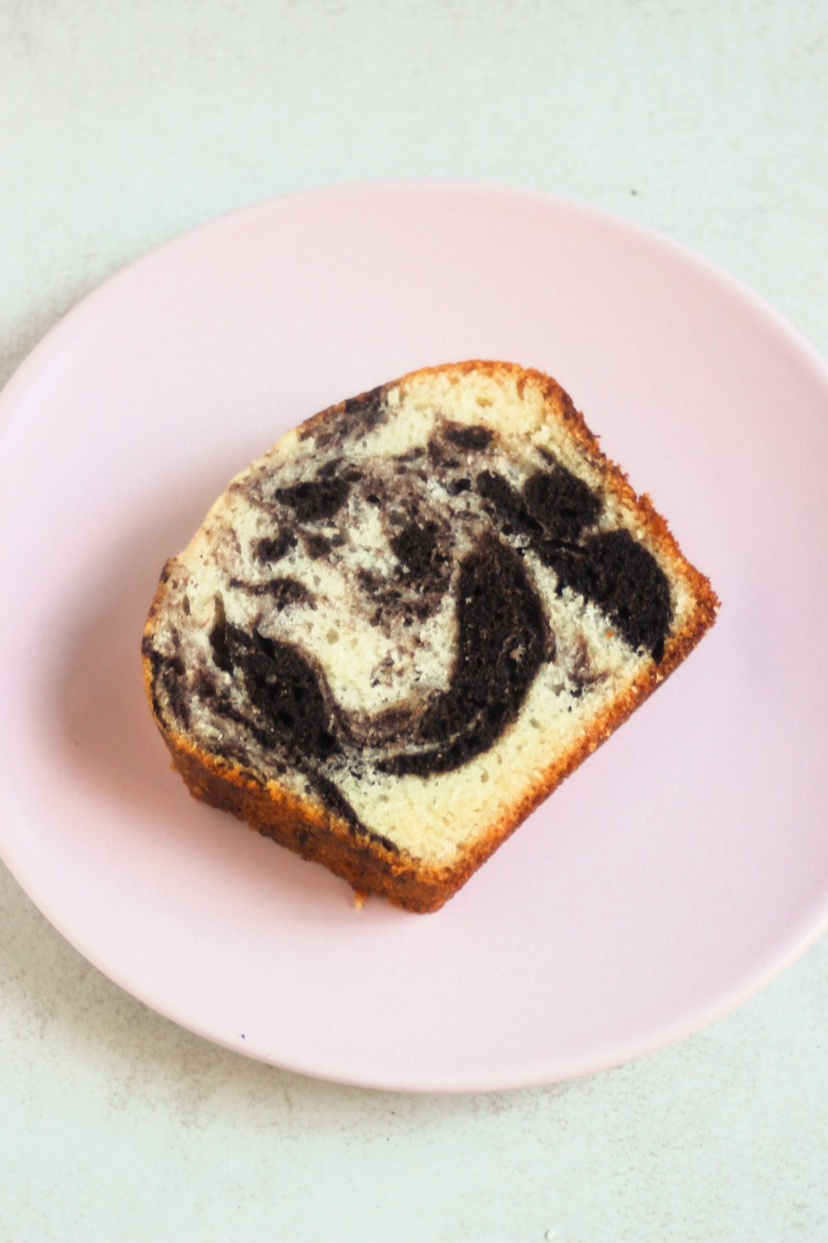 A slice of marble loaf cake on a pink plate.
