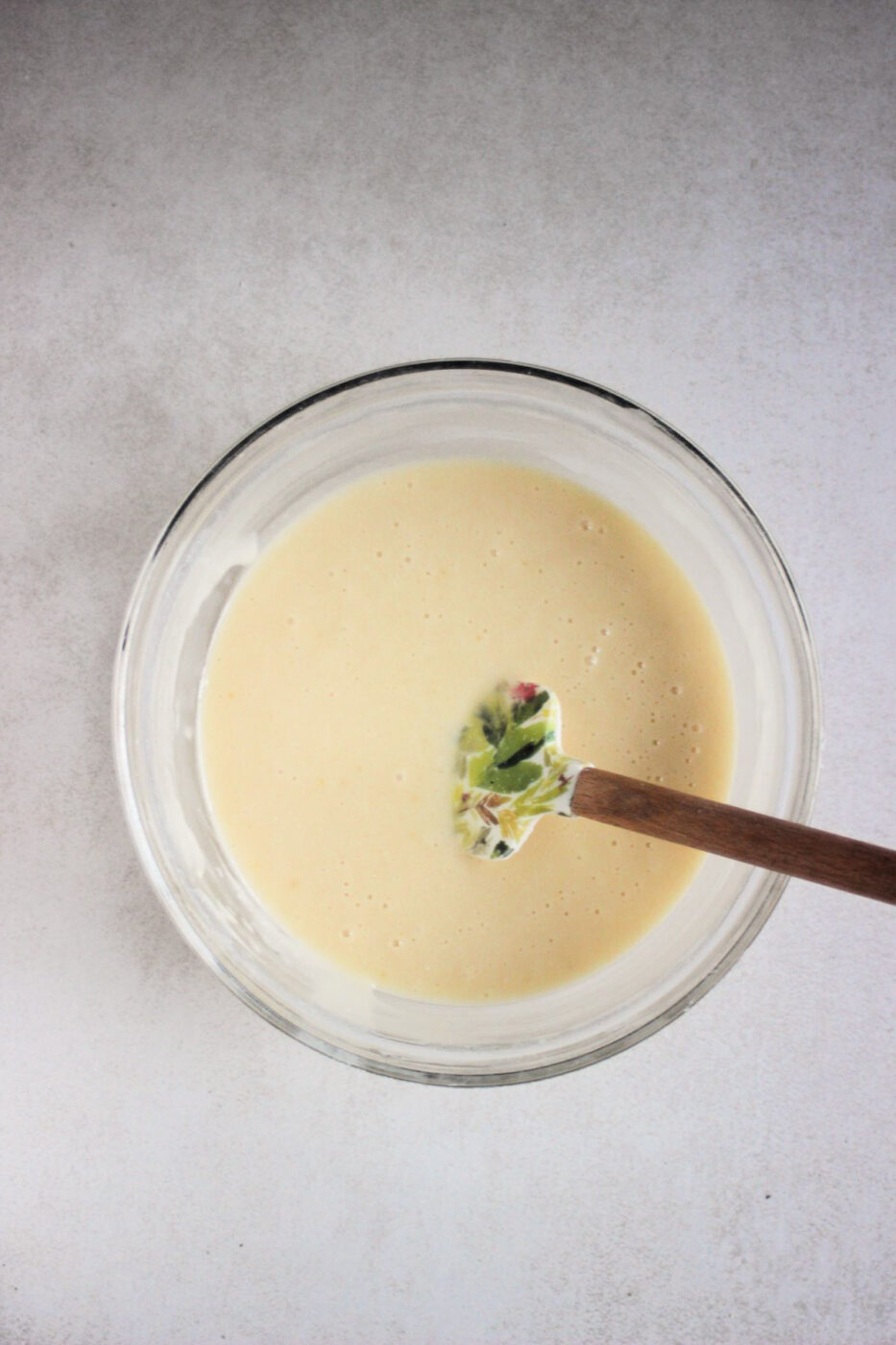 Glass bowl with a cream colour mixture and a rubber spatula.