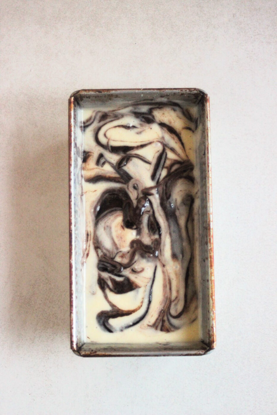 Loaf cake pan with a cream color and brown mixture seen from above.