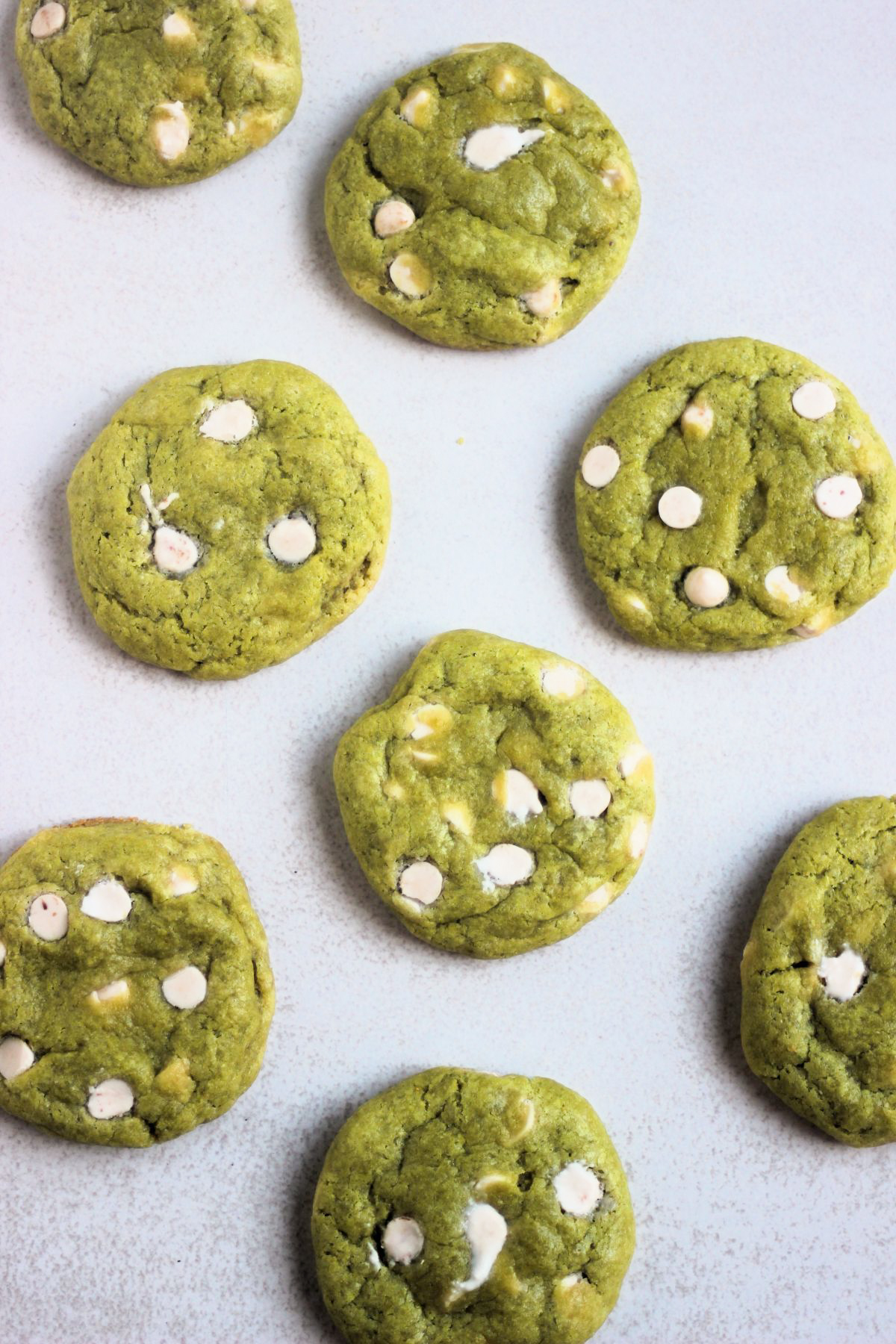 Matcha cookies with white chocolate chips on a white surface seen from above.