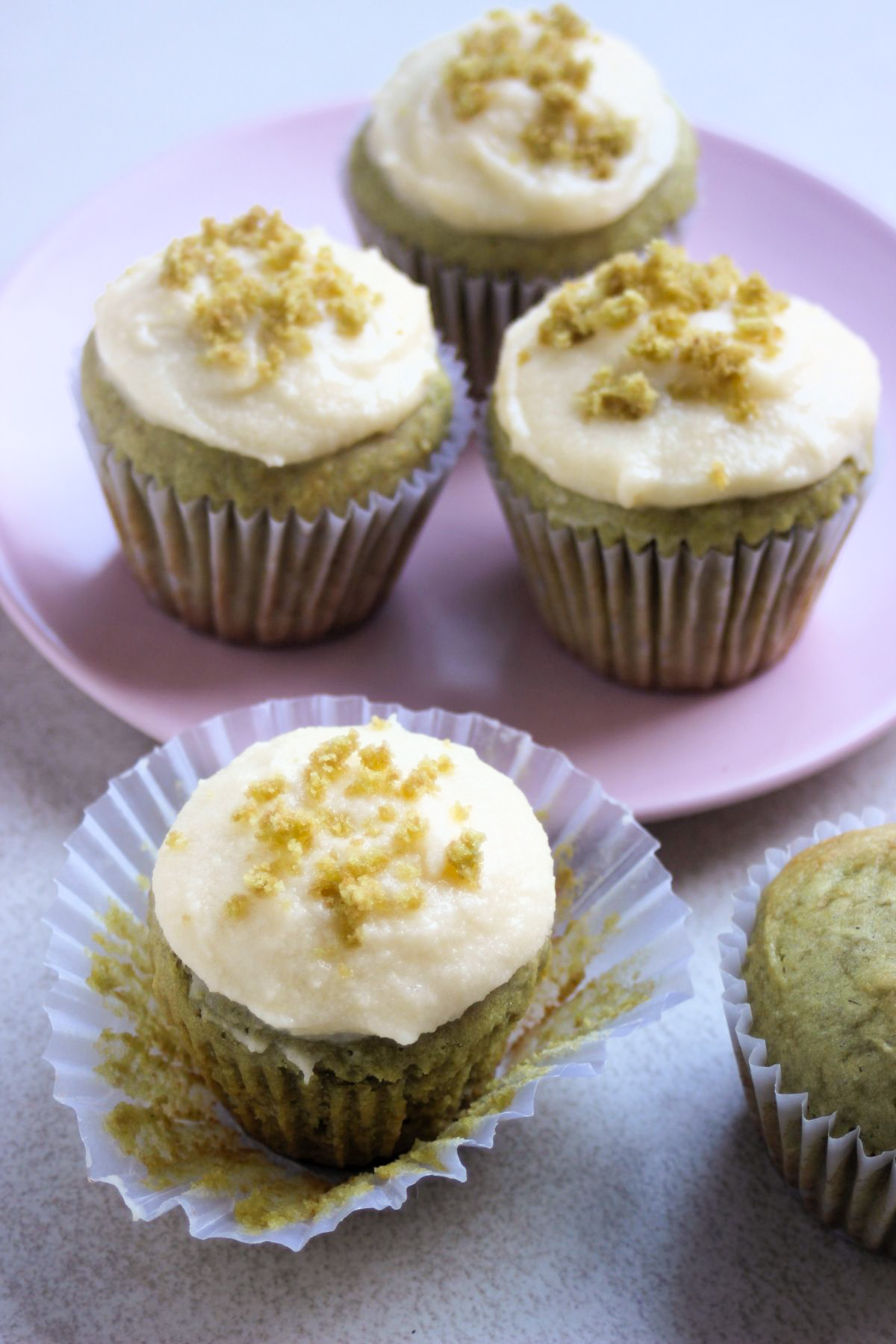 Matcha cupcake with the liner open. Behind, more cupcakes on a pink plate.