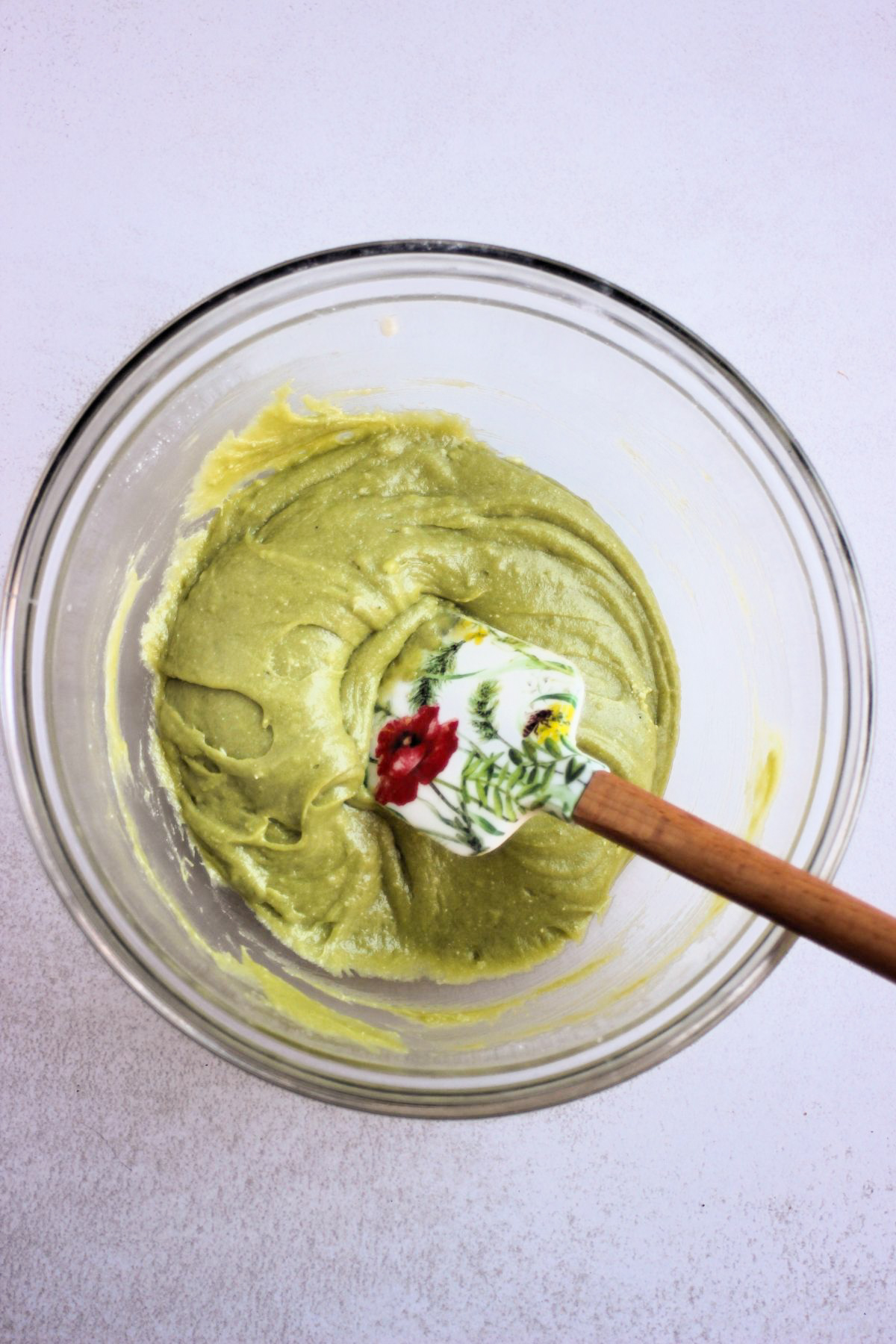 Glass bowl with a smooth, green mixture and a rubber spatula.