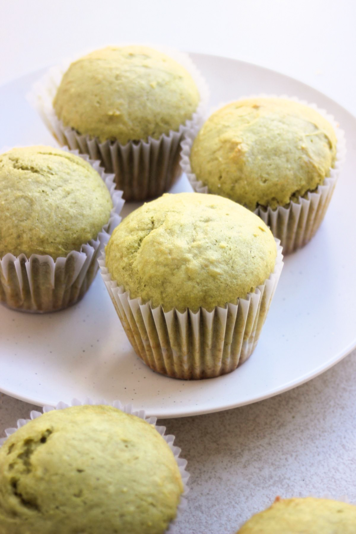 Matcha muffins with liners on a white plate.