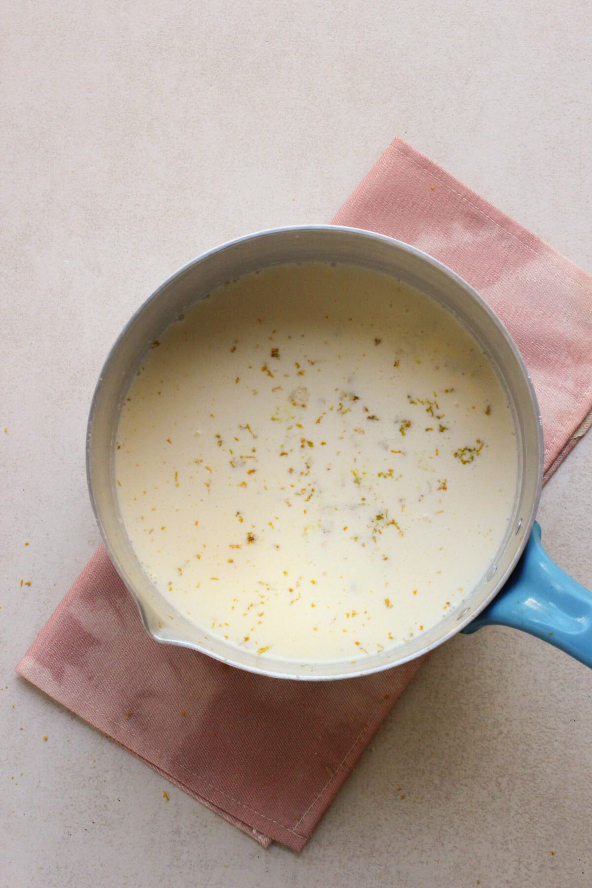 Deep saucepan with milk and orange zest.