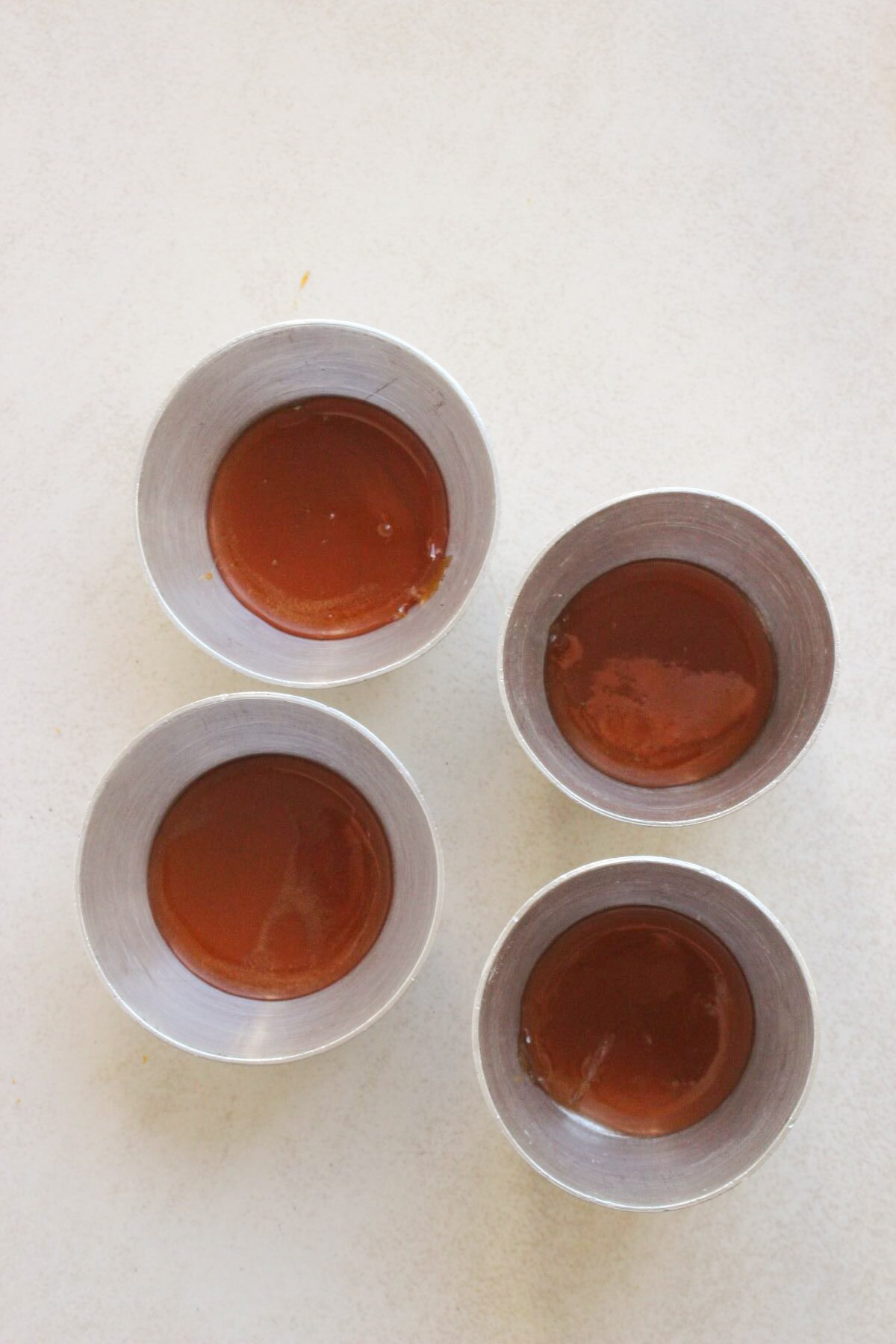 Four individual flan molds with caramel on a white surface.
