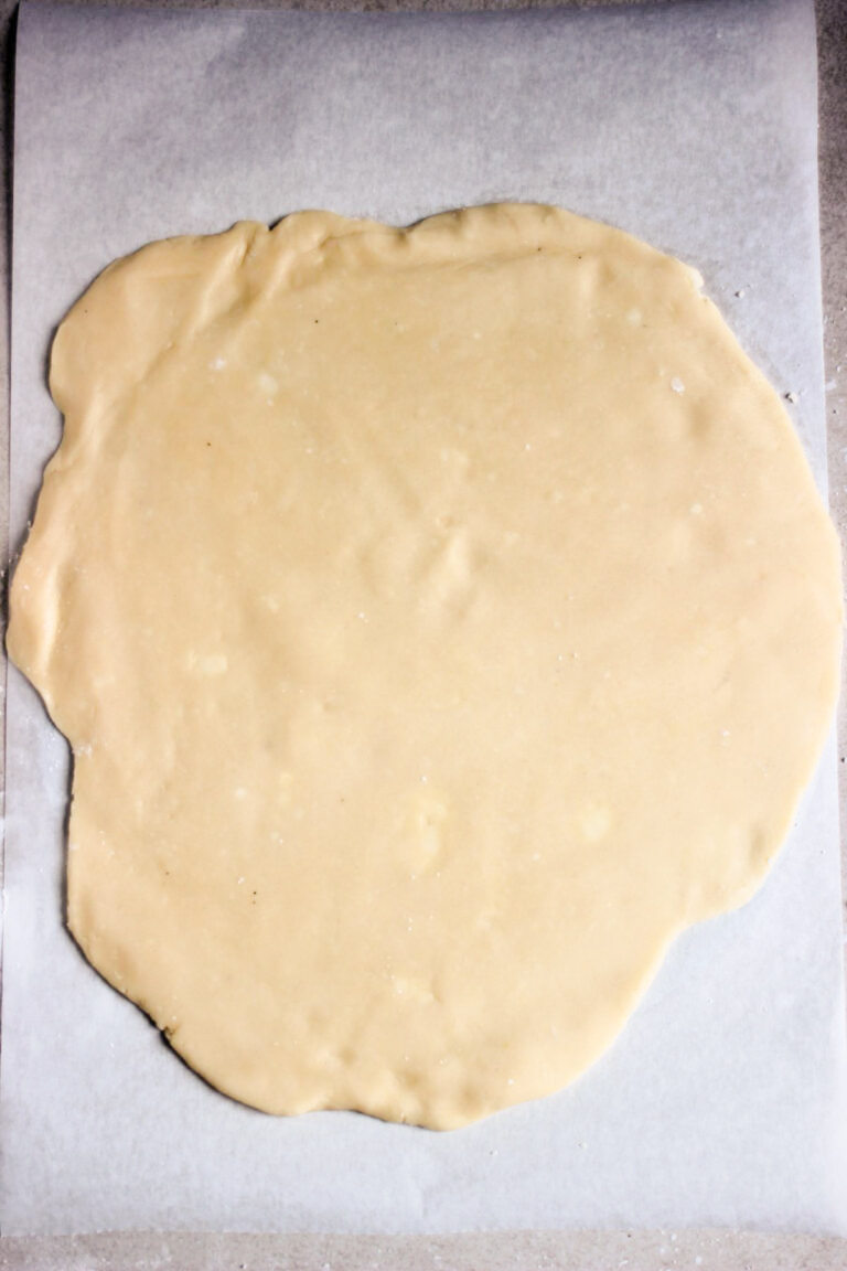 Stretched dough on a piece of parchment paper.