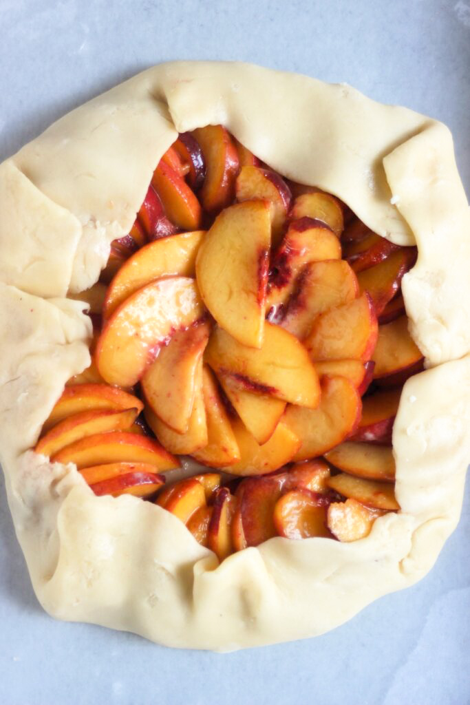 Raw peach galette on a parchment paper.