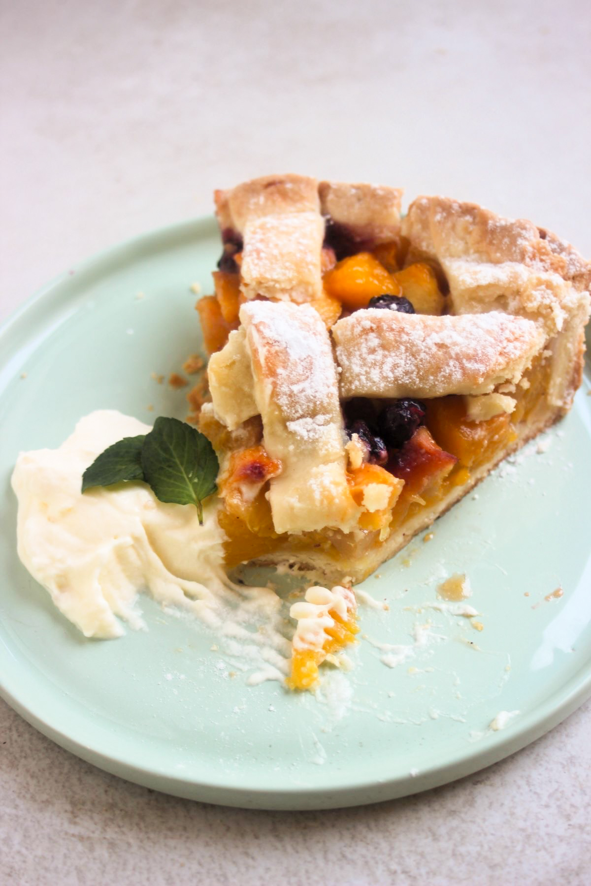 Peach pie portion without a piece with whipped cream on an aqua-green plate.