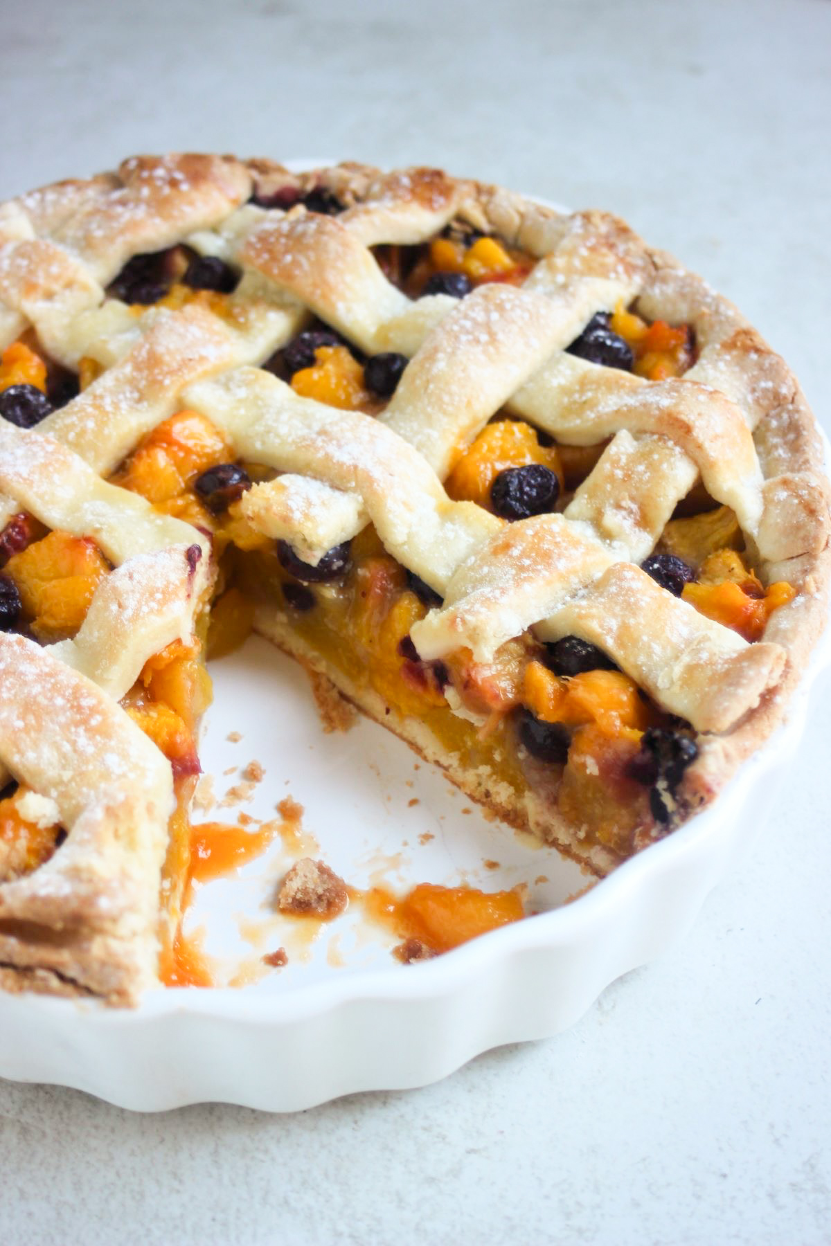 Peach pie in a round white baking dish without a portion on a grey surface.