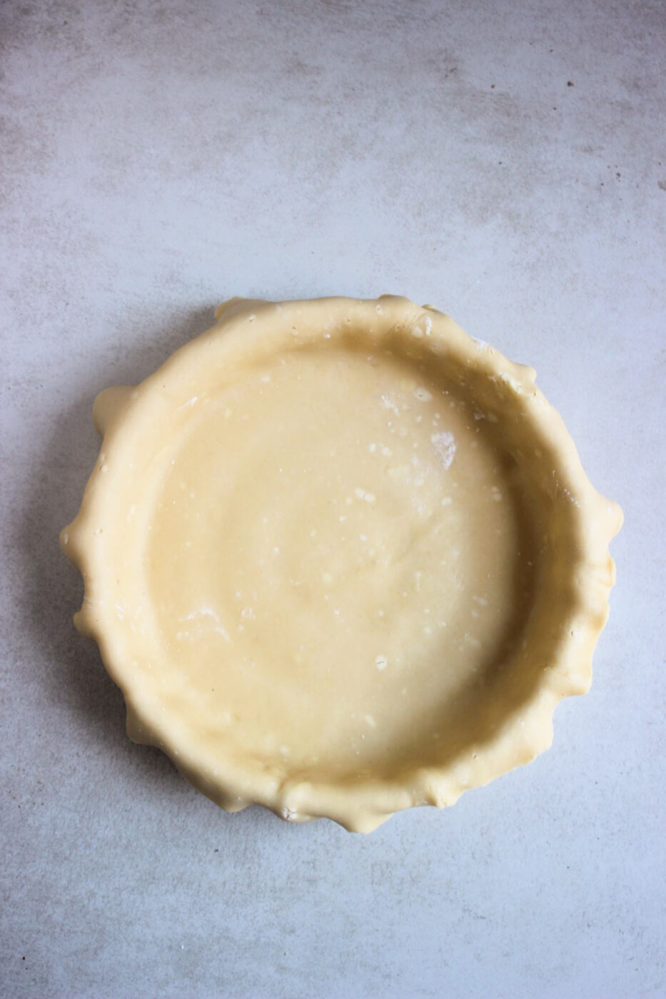 Peach pie raw batter on a round baking dish on a grey surface seen from above.