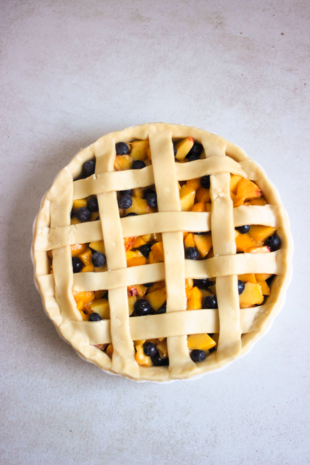 Raw peach pie in a round baking dish on a grey surface seen from above.