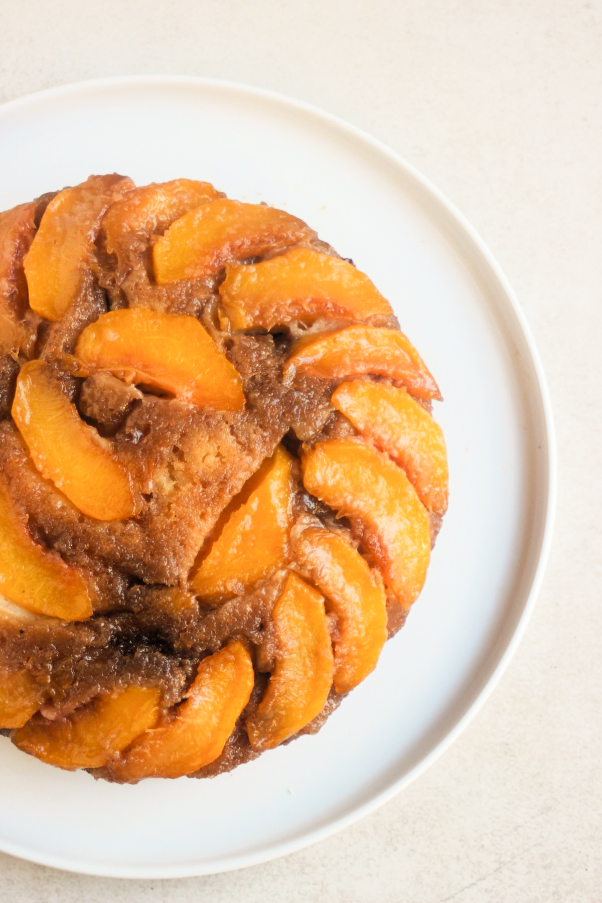 Partial view of peach upside down cake on a white plate.