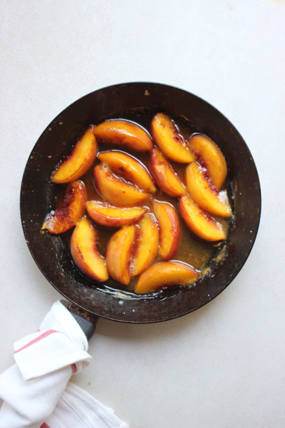 A skillet with peach slices and juice.