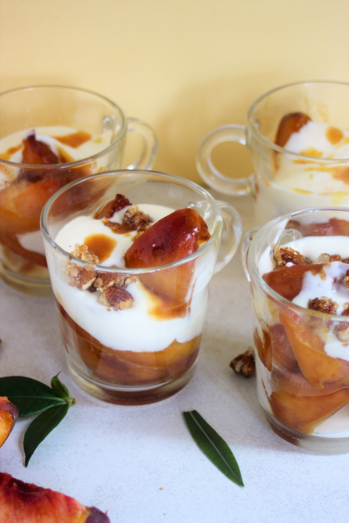 Four peach yogurt trifles in glass cups on a white surface. Green leaves on the sides.